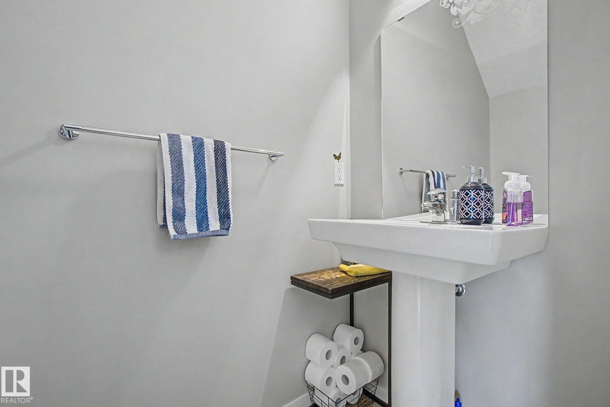 Pedestal sink with chrome faucet, large wall-mounted mirror, and a towel bar - 17 320 Secord Boulevard, Edmonton, AB - Indoor