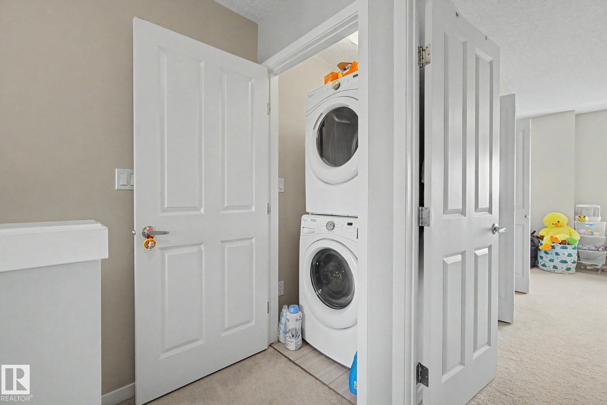 Dedicated laundry closet featuring a stacked washer and dryer unit - 17 320 Secord Boulevard, Edmonton, AB - Indoor Photo Showing Laundry Room