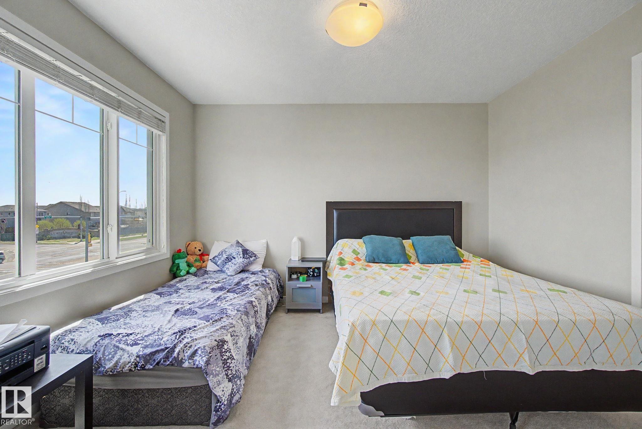 Bright room featuring a large window, neutral wall paint, and light-colored carpeting - 17 320 Secord Boulevard, Edmonton, AB - Indoor Photo Showing Bedroom