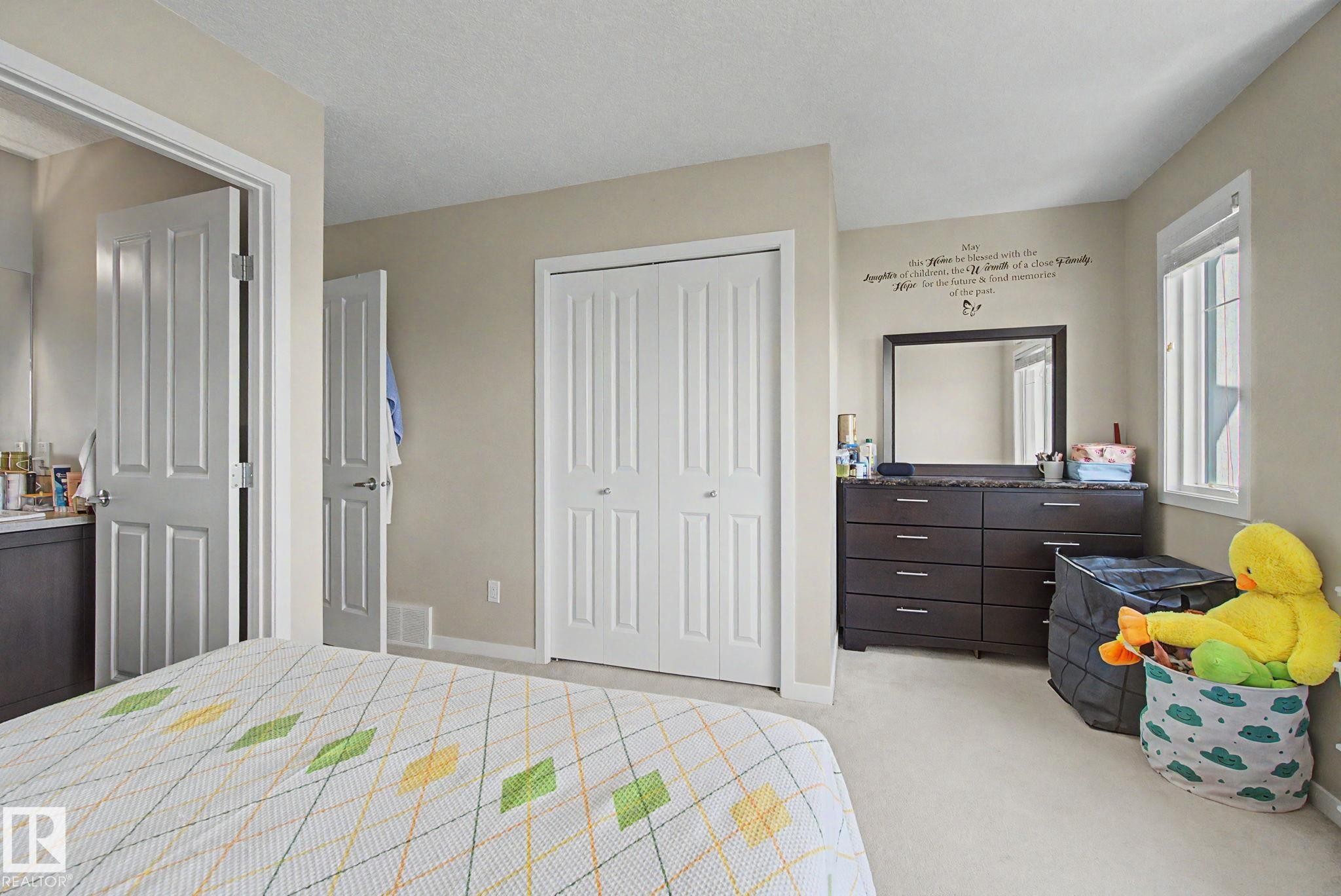 Bedroom featuring neutral-toned walls, light-colored carpeting, a window with natural light, and a bi-fold closet - 17 320 Secord Boulevard, Edmonton, AB - Indoor Photo Showing Bedroom