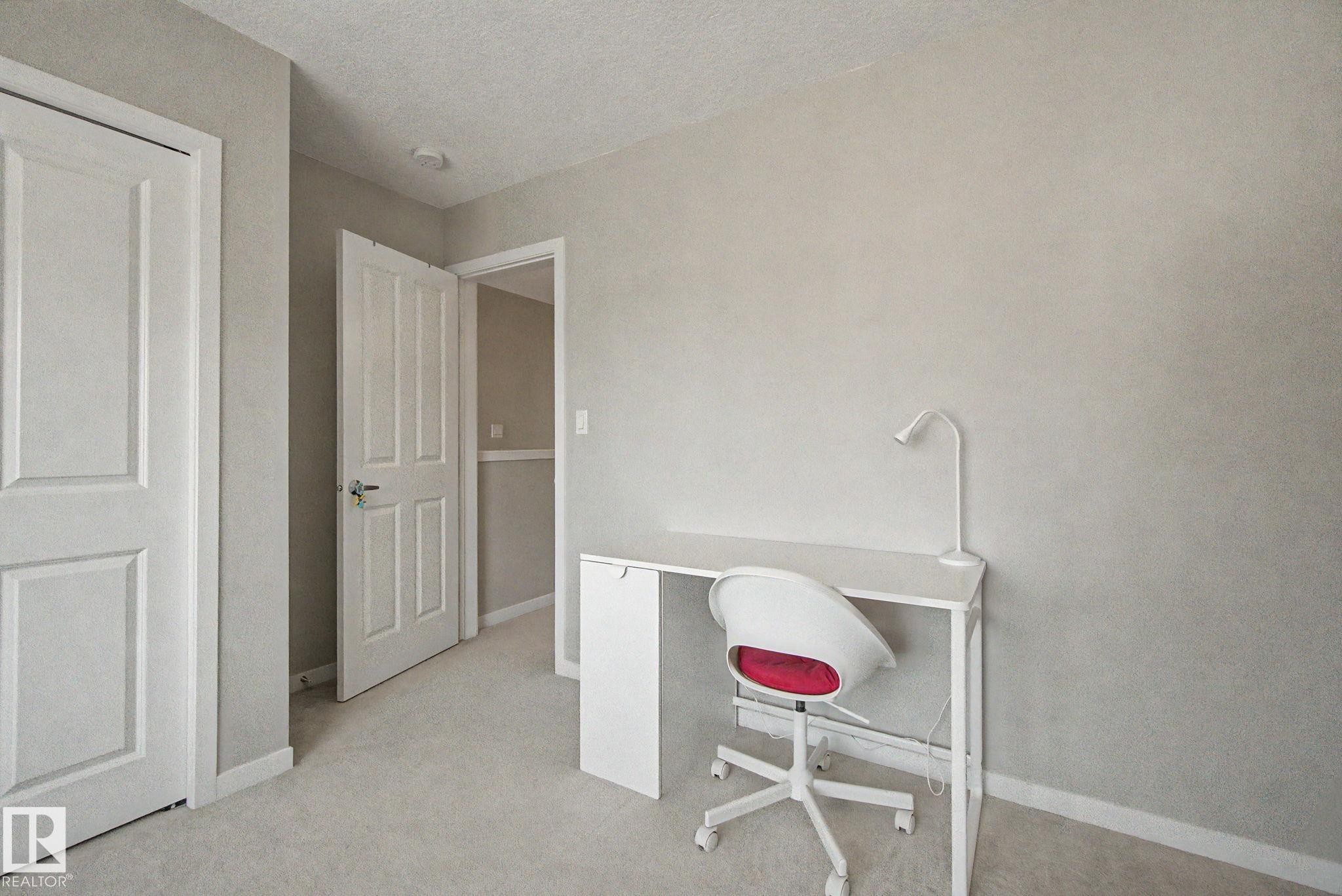 Carpeted room featuring a neutral color palette, white trim, and a white paneled door - 17 320 Secord Boulevard, Edmonton, AB - Indoor