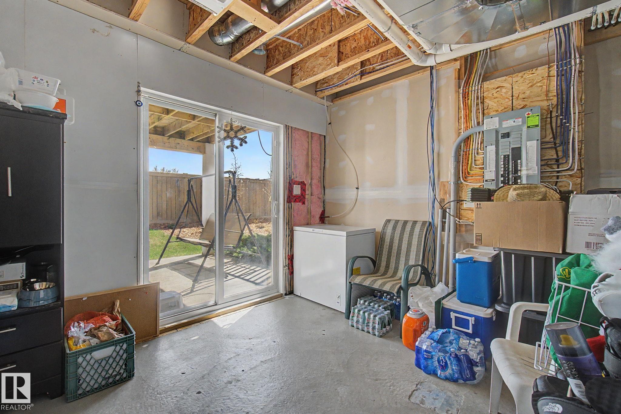 Unfinished basement space featuring exposed ceiling joists and ductwork, a sliding glass door providing exterior access, and a concrete floor - 17 320 Secord Boulevard, Edmonton, AB - Indoor Photo Showing Other Room