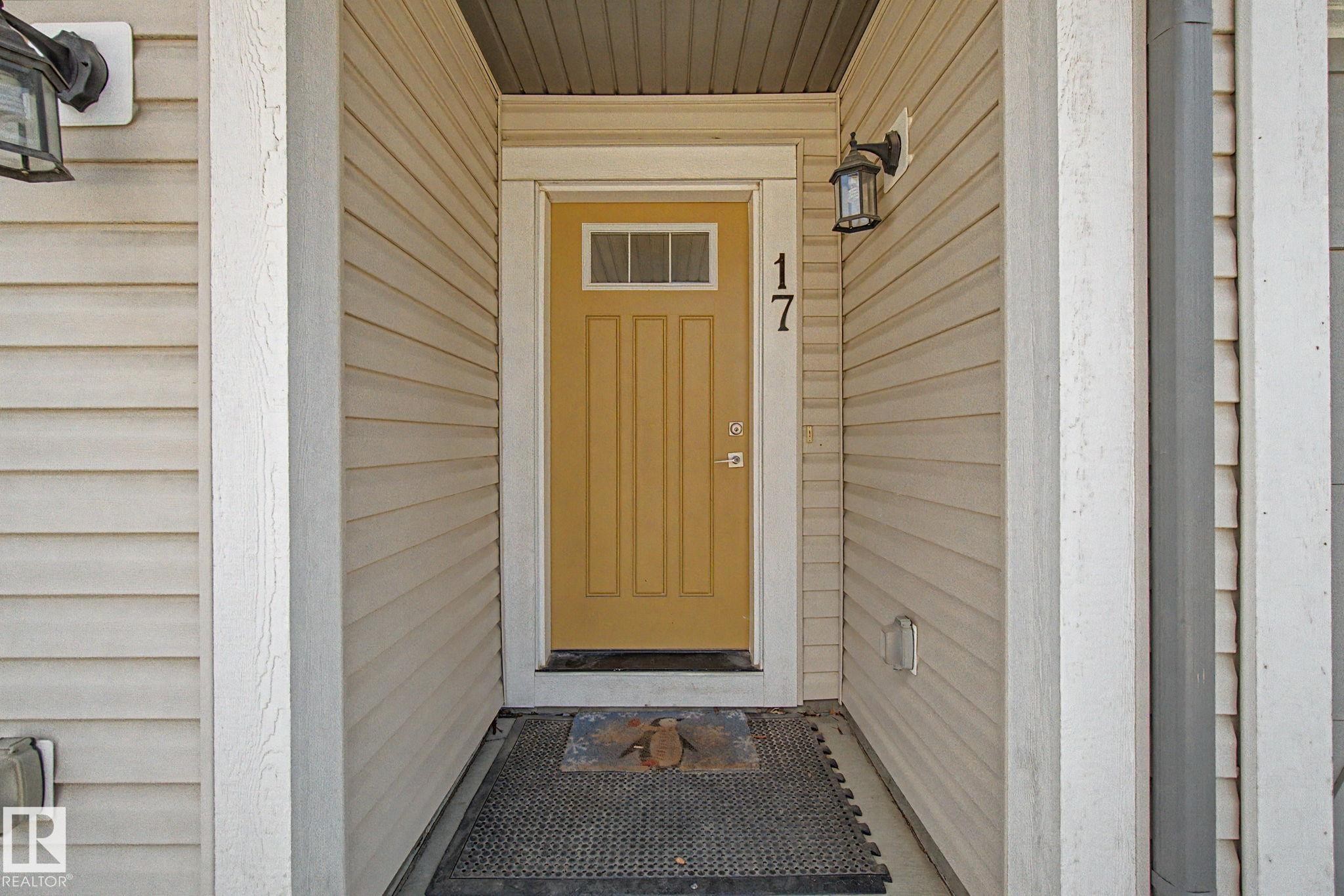 Welcoming entry featuring a bright yellow door with upper glass panes, flanked by two outdoor wall sconces - 17 320 Secord Boulevard, Edmonton, AB - Outdoor With Exterior