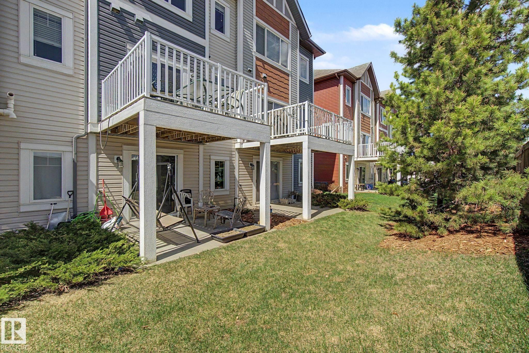 Rear exterior showcasing a private upper-level balcony, a ground-level patio, and a manicured lawn - 17 320 Secord Boulevard, Edmonton, AB - Outdoor