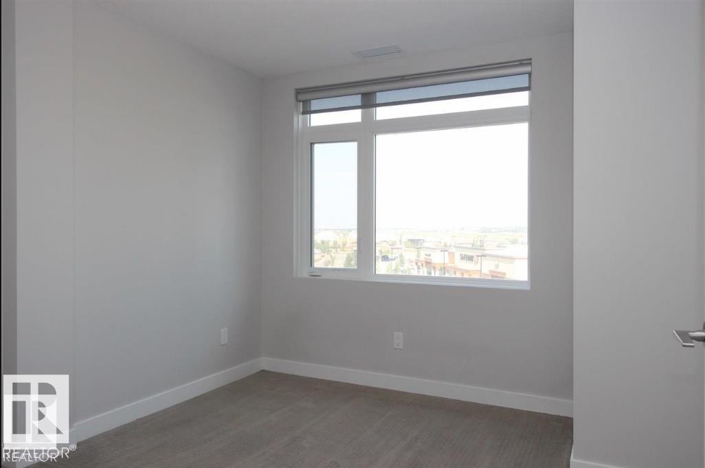 Bright room featuring a large window, neutral wall paint, white baseboards, and gray carpet flooring - 531 5151 Windermere Boulevard, Edmonton, AB - Indoor Photo Showing Other Room