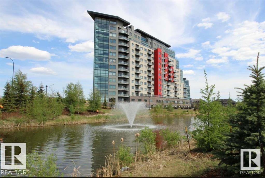 Modern high-rise building featuring a striking red facade accent, glass curtain wall elements, and private balconies - 531 5151 Windermere Boulevard, Edmonton, AB - Outdoor With Body Of Water With Facade