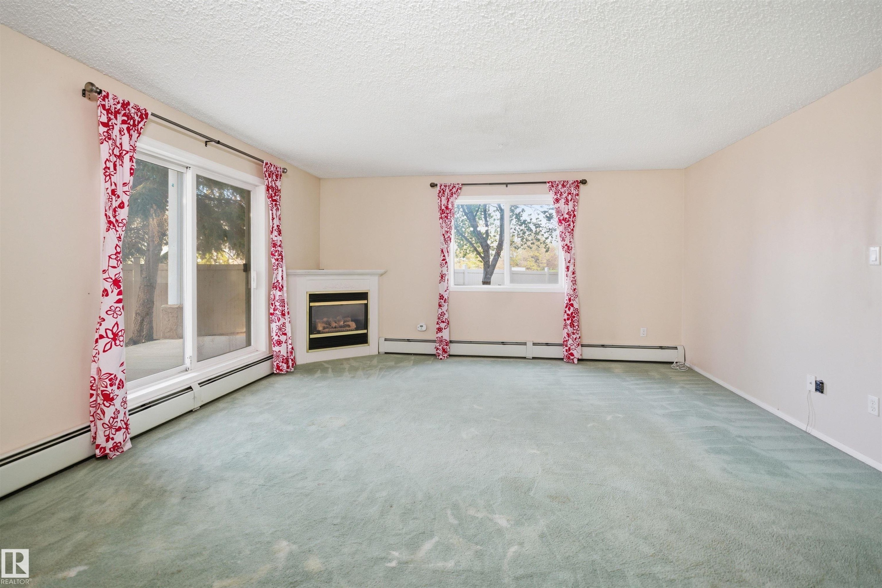 Spacious room featuring light-colored walls, a corner fireplace with a white mantel, and a sliding glass door providing exterior access - 124 10511 42 Avenue, Edmonton, AB