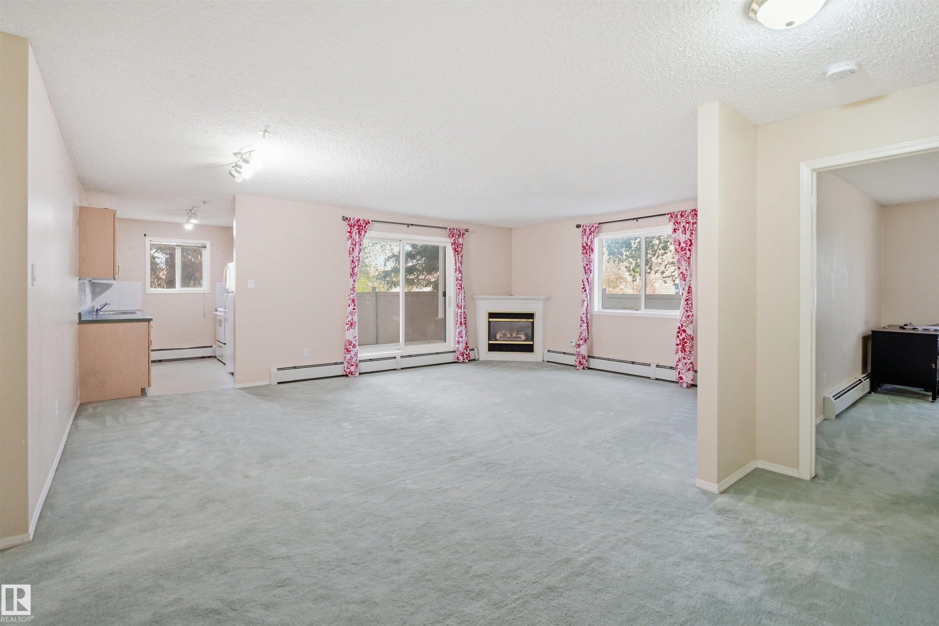 Open concept living area featuring light-colored carpeting, a fireplace with a white mantel, and a sliding glass door - 124 10511 42 Avenue, Edmonton, AB