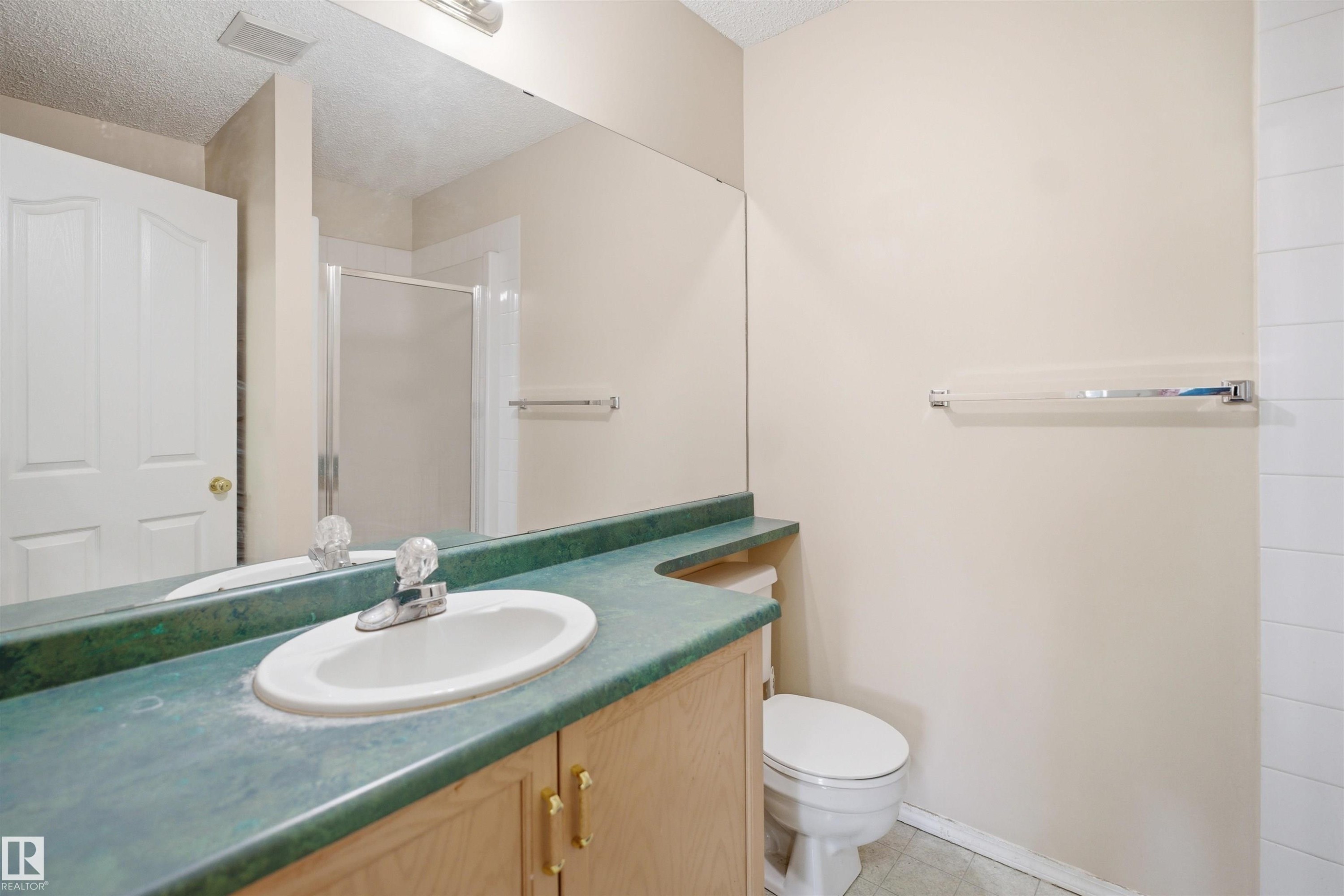 Bathroom featuring a single vanity with a green countertop, light wood-finish cabinetry, an integrated sink, and an expansive wall mirror - 124 10511 42 Avenue, Edmonton, AB