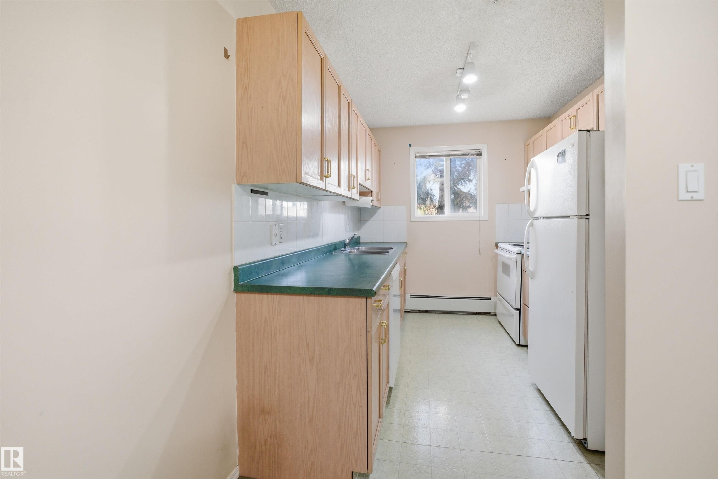Galley kitchen featuring wood-finish cabinetry, white tile backsplash, and a green countertop - 124 10511 42 Avenue, Edmonton, AB