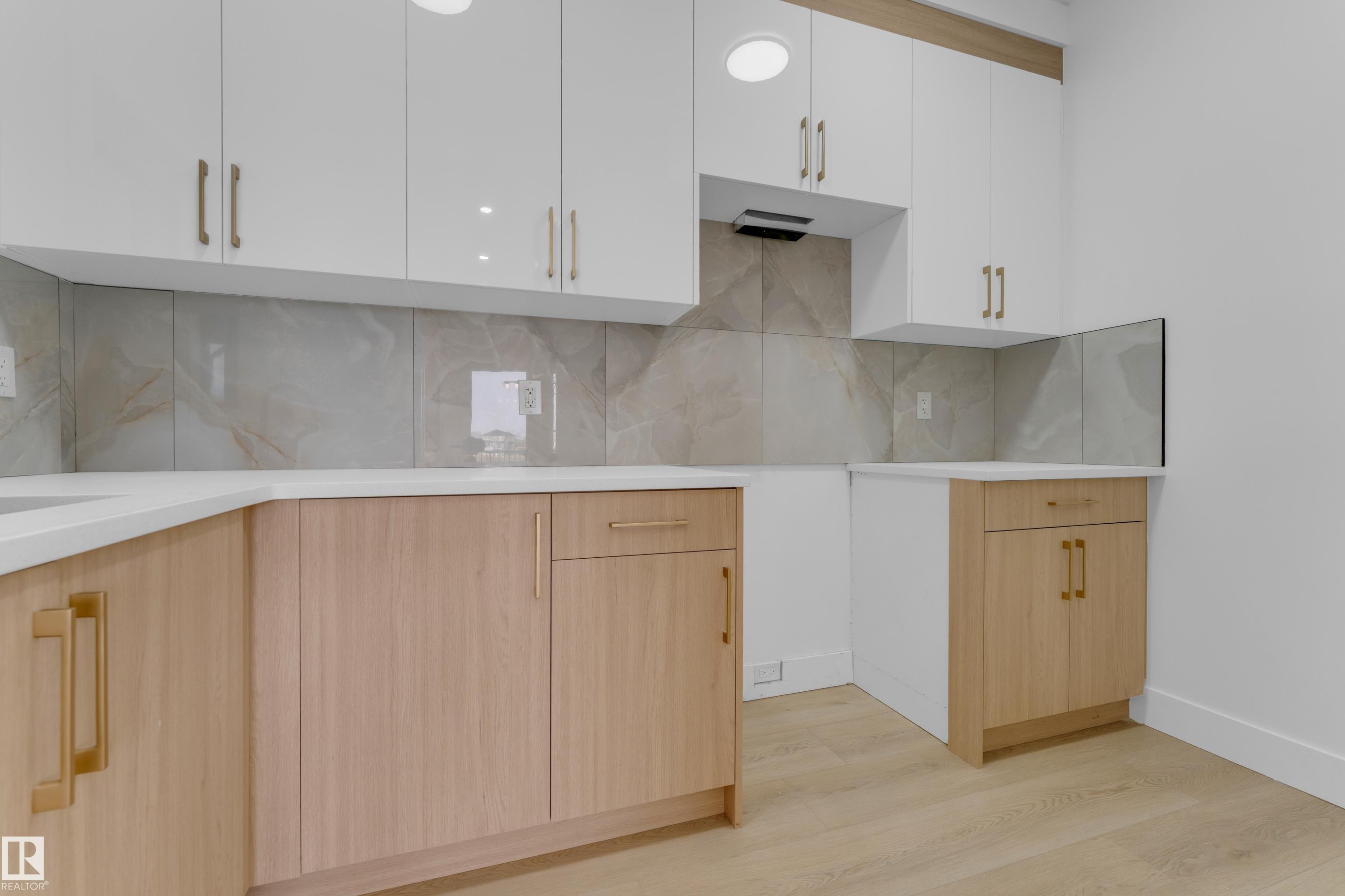 Modern kitchen featuring two-tone cabinetry with white upper cabinets and wood-finish lower cabinets, light-toned countertops, and a full tile backsplash - 449 Crystal Creek Link, Leduc, AB - Indoor Photo Showing Kitchen