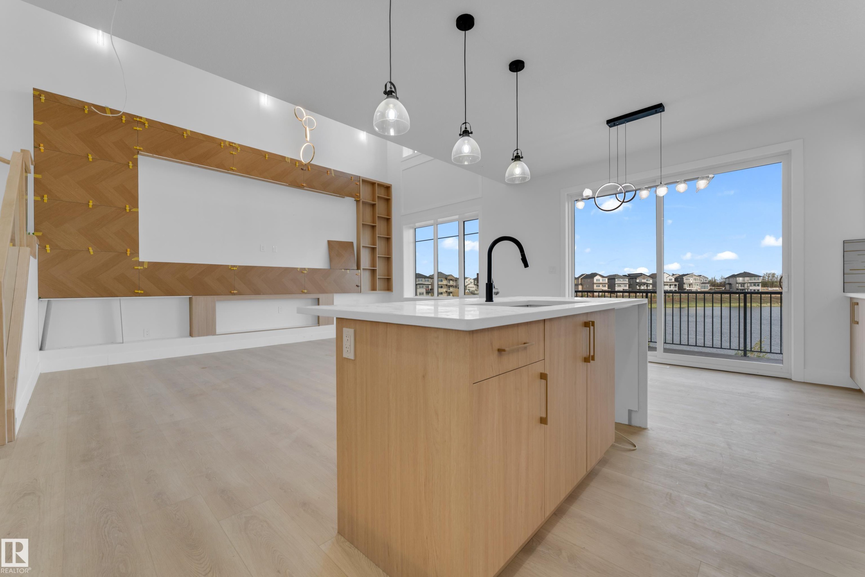 Spacious interior featuring light wood-finish flooring, a kitchen island with a white countertop and black gooseneck faucet, and a large sliding glass door opening to a balcony - 449 Crystal Creek Link, Leduc, AB - Indoor Photo Showing Kitchen