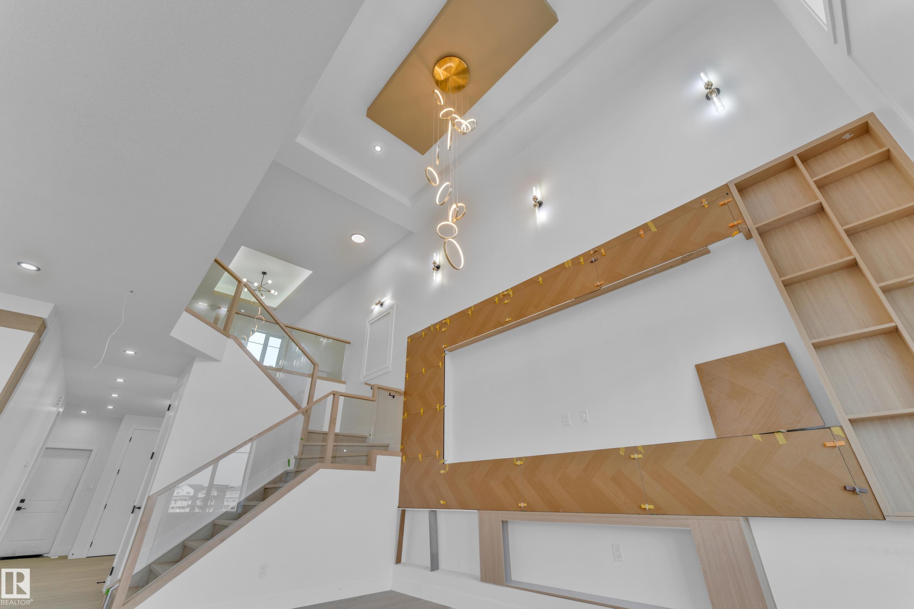 Double-height entry featuring a contemporary chandelier, recessed lighting, a modern staircase with glass railing, and a built-in shelving unit with wood-finish paneling - 449 Crystal Creek Link, Leduc, AB - Indoor Photo Showing Other Room