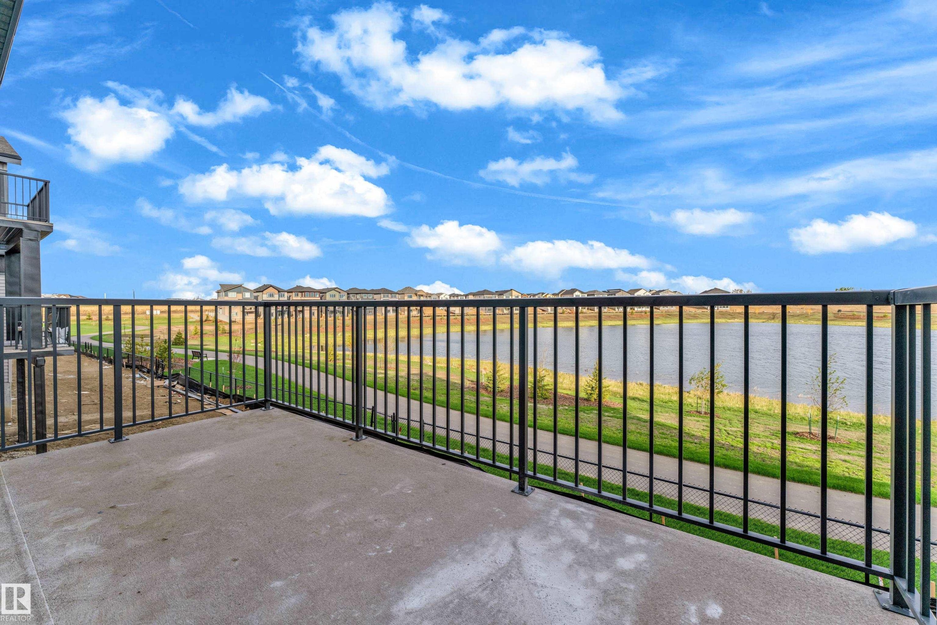 Concrete balcony with black metal railing overlooking a body of water and walking path - 449 Crystal Creek Link, Leduc, AB - Outdoor