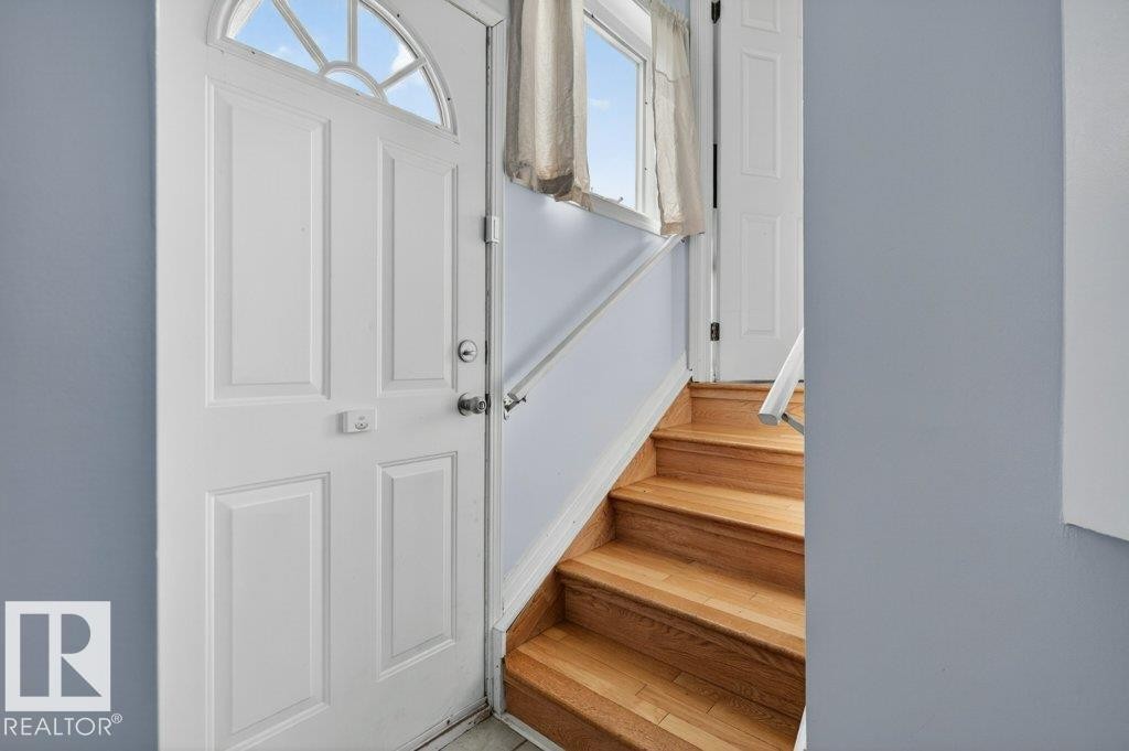Entryway featuring a white paneled door with an arched transom window, light blue wall paint, natural wood stairs, and a white handrail - 157 Kiniski Crescent, Edmonton, AB - Indoor Photo Showing Other Room