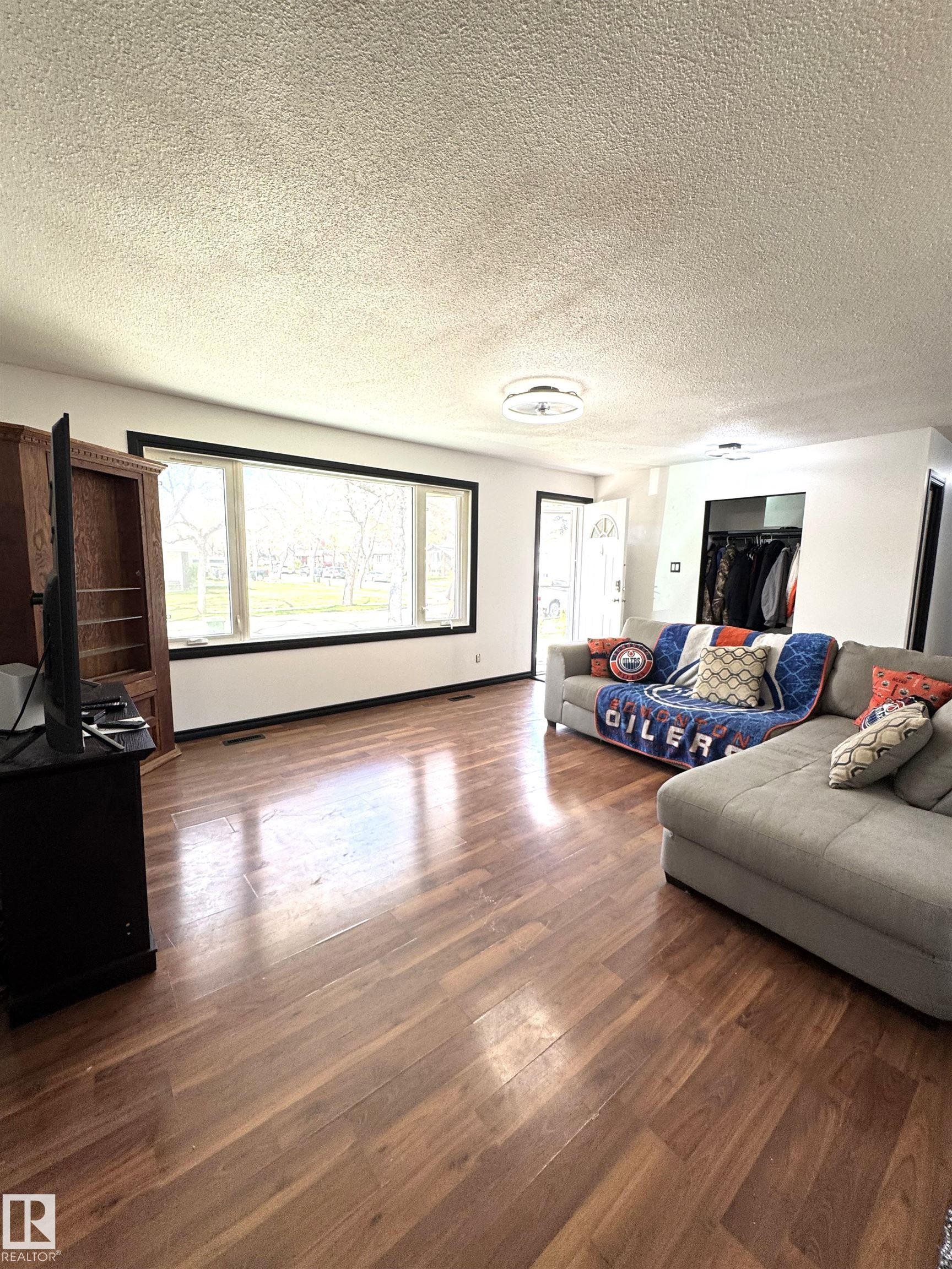 Spacious living area featuring wood-finish flooring, a large picture window with black trim, and white walls - 45 Lambert Crescent, St. Albert, AB - Indoor