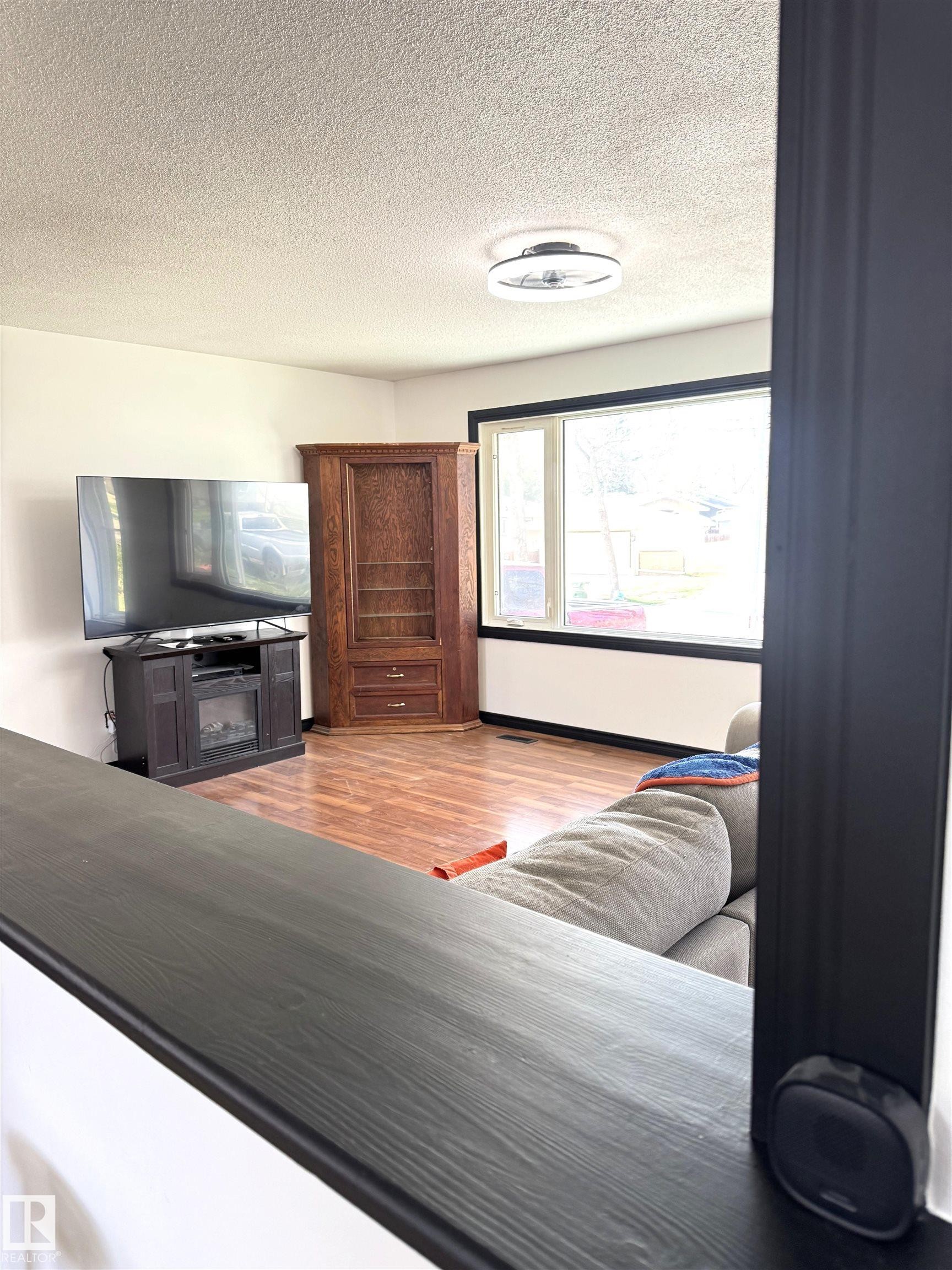 Living area featuring wood-finish flooring, a large picture window with dark trim, and a contemporary ceiling fixture - 45 Lambert Crescent, St. Albert, AB - Indoor