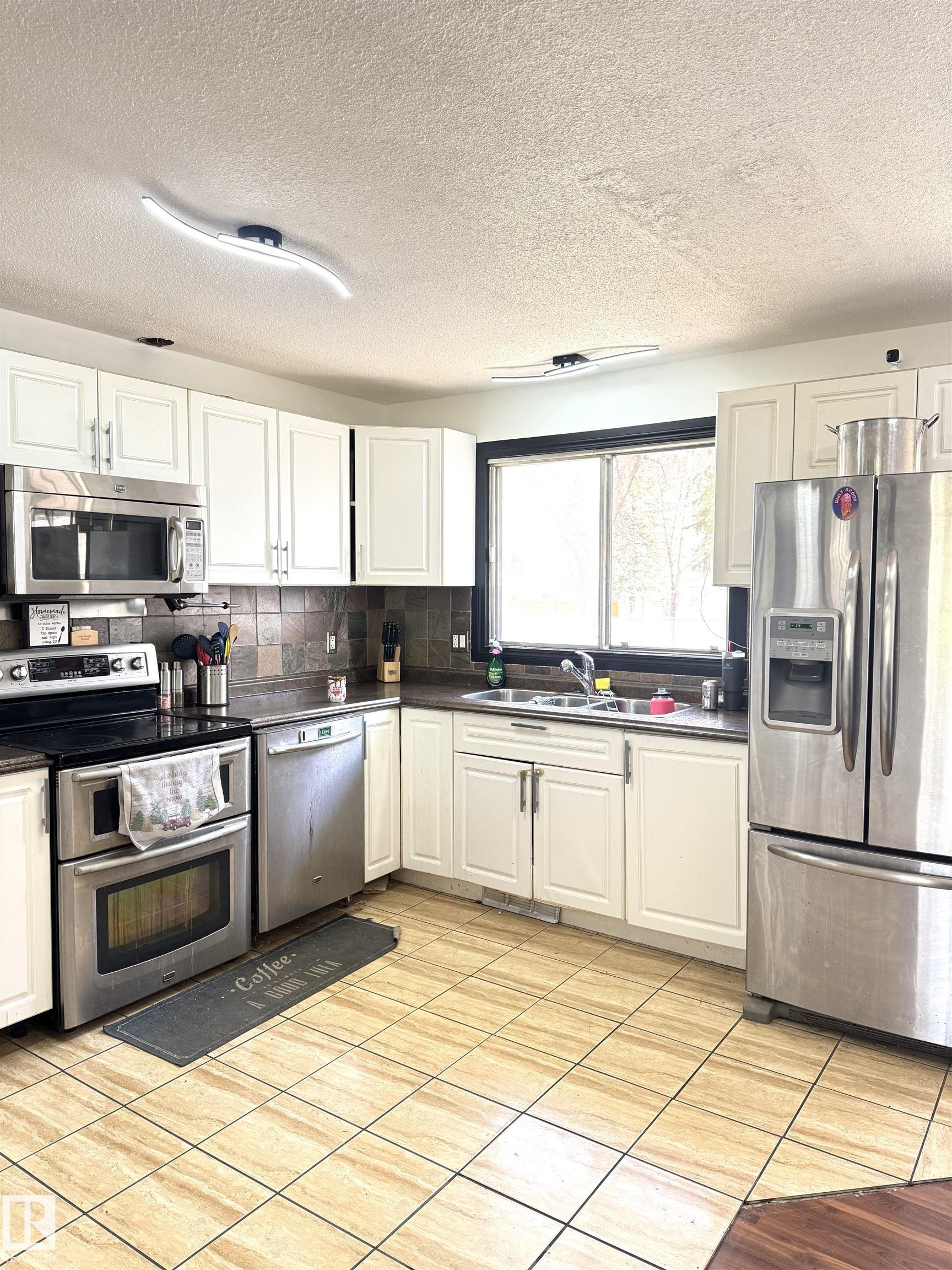 Kitchen featuring white cabinetry, stainless steel appliances, dark countertops, and a tiled backsplash - 45 Lambert Crescent, St. Albert, AB - Indoor Photo Showing Kitchen With Double Sink