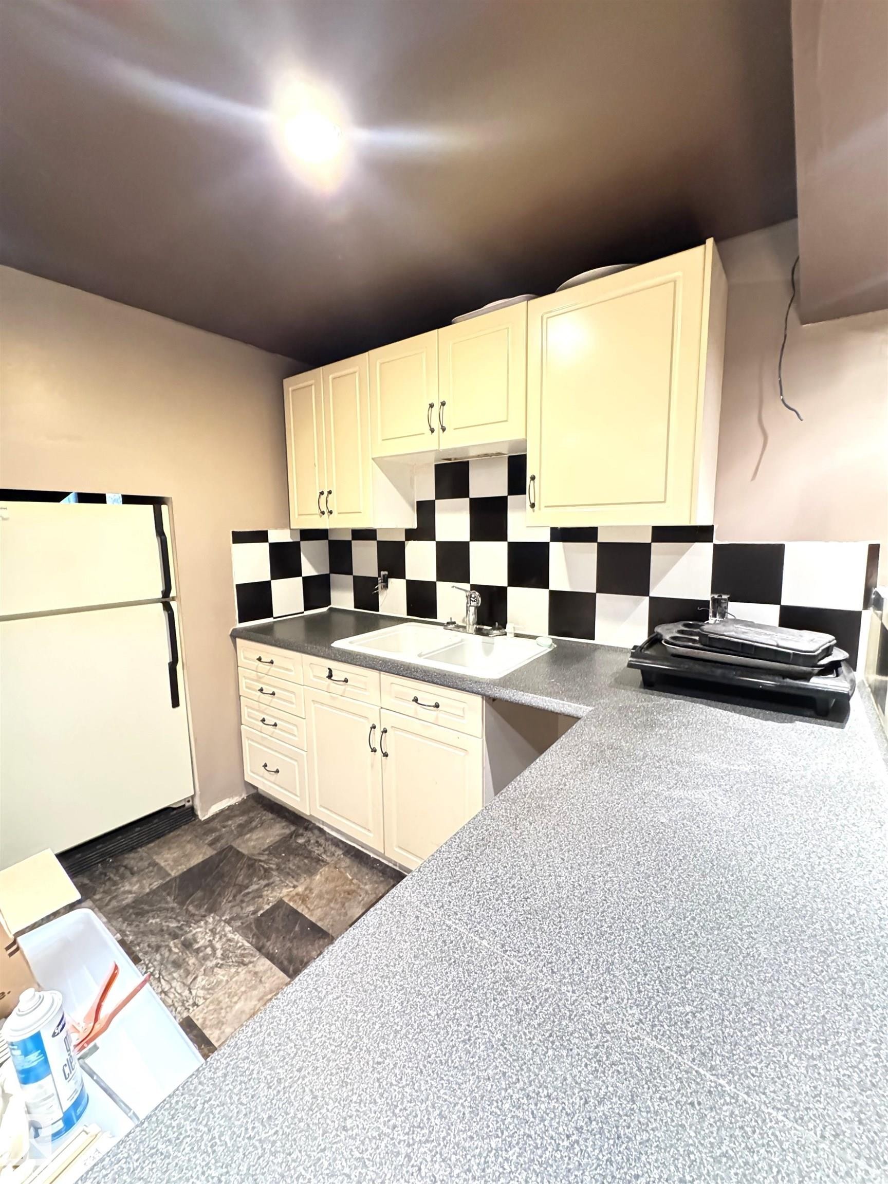 Kitchen featuring light-toned cabinetry, a double basin sink, black and white checkered backsplash, speckled countertops, and dark-toned flooring - 45 Lambert Crescent, St. Albert, AB - Indoor