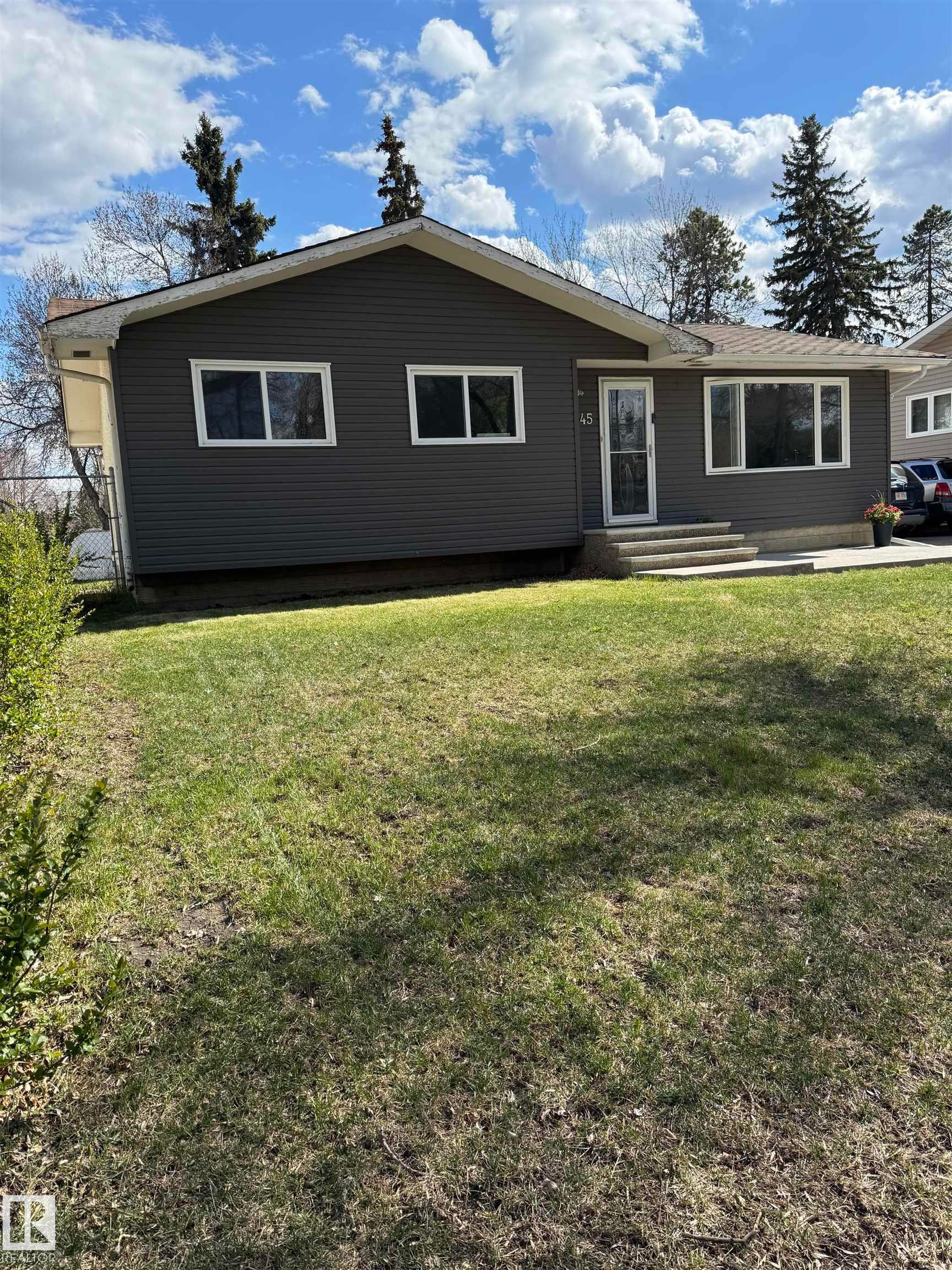 Ranch-style residence featuring dark gray horizontal siding, white trim, and a prominent front lawn - 45 Lambert Crescent, St. Albert, AB - Outdoor