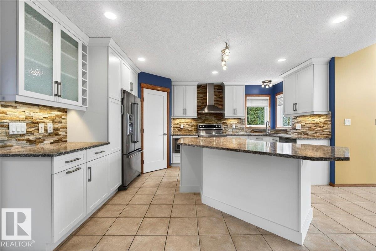 Kitchen featuring white cabinetry, stone tile backsplash, stainless steel appliances, granite countertops, and tile flooring - 11824 13 Avenue, Edmonton, AB - Indoor Photo Showing Kitchen With Upgraded Kitchen