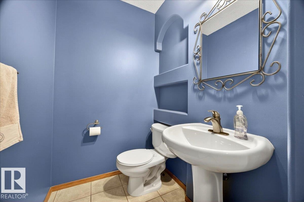 Powder room featuring a pedestal sink with a brushed nickel faucet, an ornate wall mirror, and integrated wall shelving - 11824 13 Avenue, Edmonton, AB - Indoor Photo Showing Bathroom