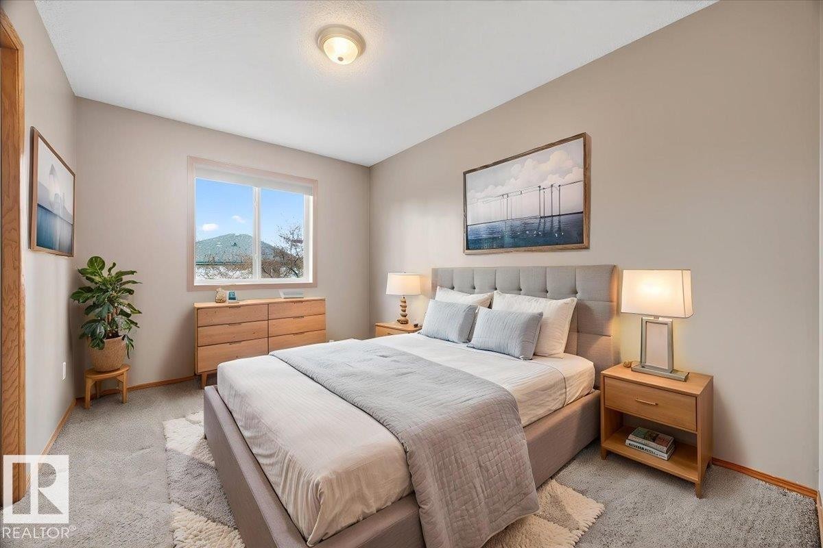 Carpeted bedroom featuring a large window, neutral wall tones, baseboard trim, and a ceiling-mounted light fixture - 11824 13 Avenue, Edmonton, AB - Indoor Photo Showing Bedroom