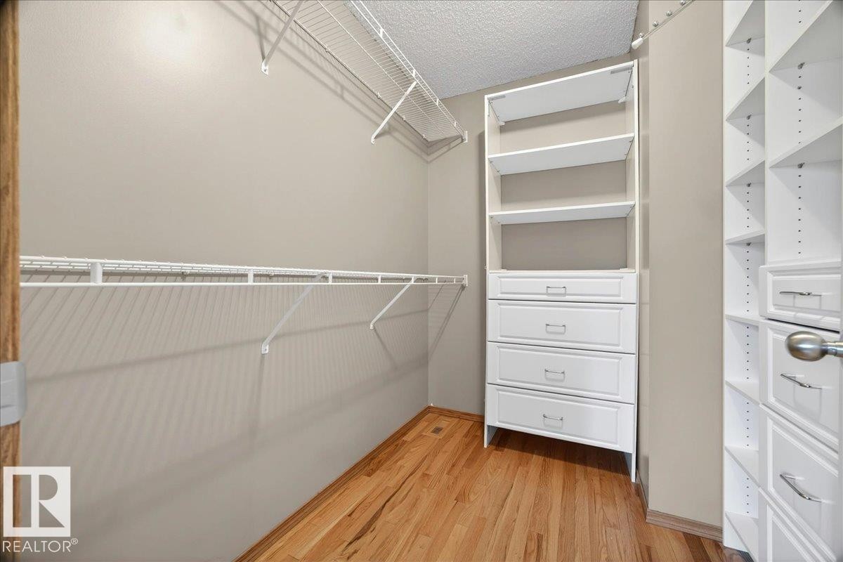 Walk-in closet featuring wood-finish flooring, neutral wall tones, white wire shelving, and built-in white cabinetry with drawers and open shelving units - 11824 13 Avenue, Edmonton, AB - Indoor With Storage