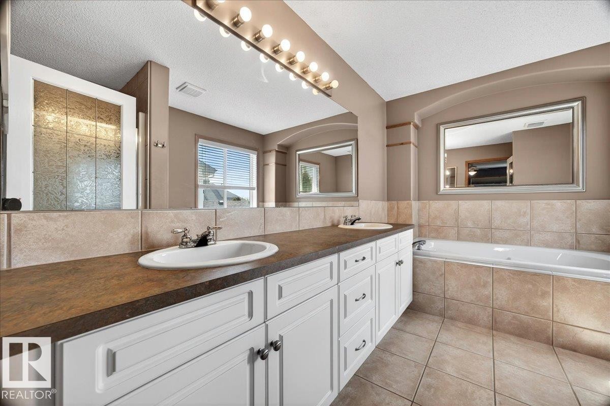 Dual vanity with integrated sinks, white cabinetry, dark countertop, and tiled backsplash - 11824 13 Avenue, Edmonton, AB - Indoor Photo Showing Bathroom
