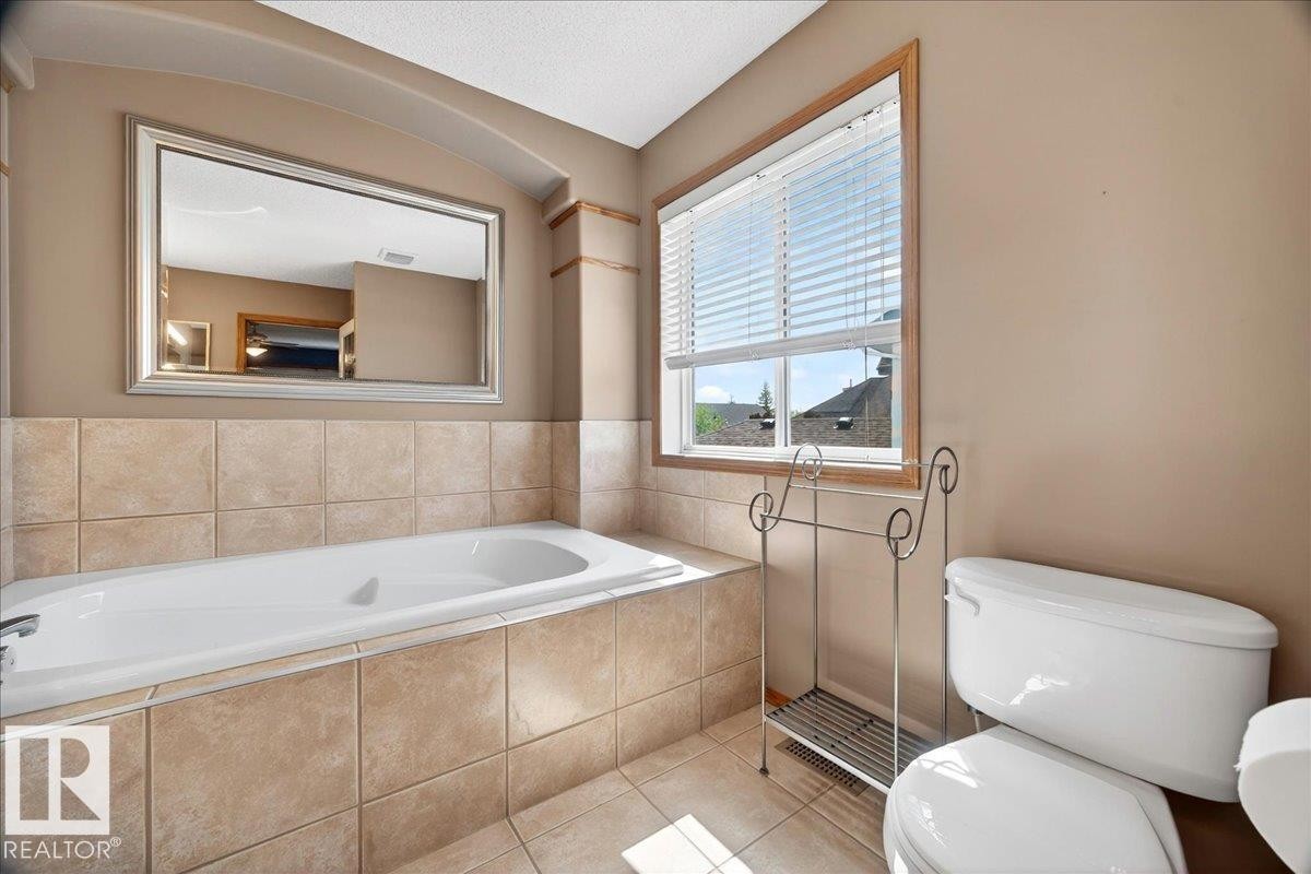 Bathroom featuring a built-in soaking tub, extensive tile surround, and a framed wall mirror - 11824 13 Avenue, Edmonton, AB - Indoor Photo Showing Bathroom