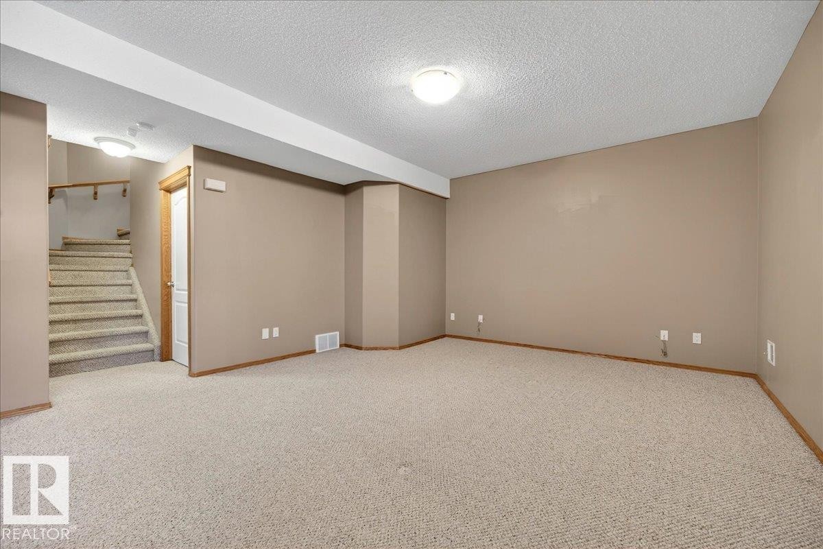 Spacious carpeted room featuring a neutral color palette, recessed lighting, and a visible staircase with wood-finish railing - 11824 13 Avenue, Edmonton, AB - Indoor