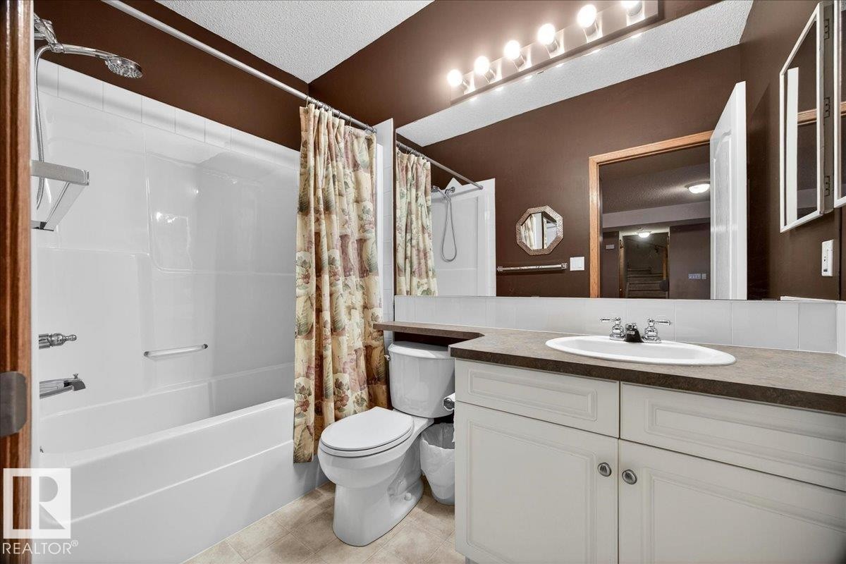 Bathroom featuring an integrated tub and shower unit, white vanity with dual cabinet storage, drop-in sink, and a full-width mirror - 11824 13 Avenue, Edmonton, AB - Indoor Photo Showing Bathroom