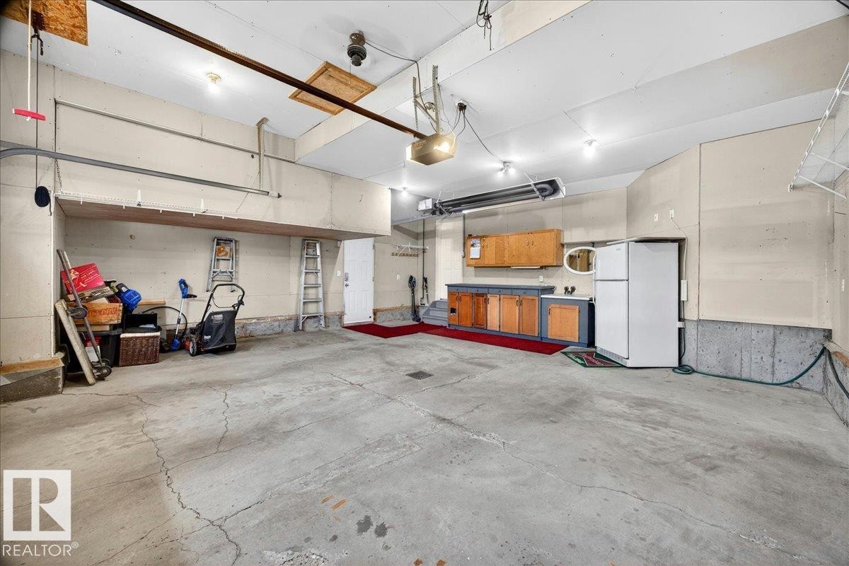 Spacious garage featuring a concrete floor, overhead lighting, an exposed ceiling, and a built-in utility sink with cabinetry - 11824 13 Avenue, Edmonton, AB - Indoor Photo Showing Garage