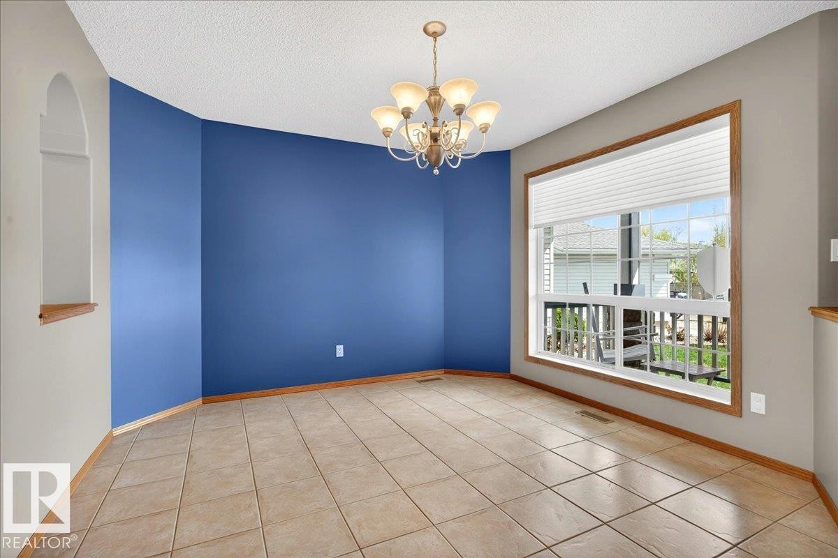Spacious room featuring tile flooring, a large window with white blinds, a multi-arm chandelier, and an arched wall niche - 11824 13 Avenue, Edmonton, AB - Indoor Photo Showing Other Room