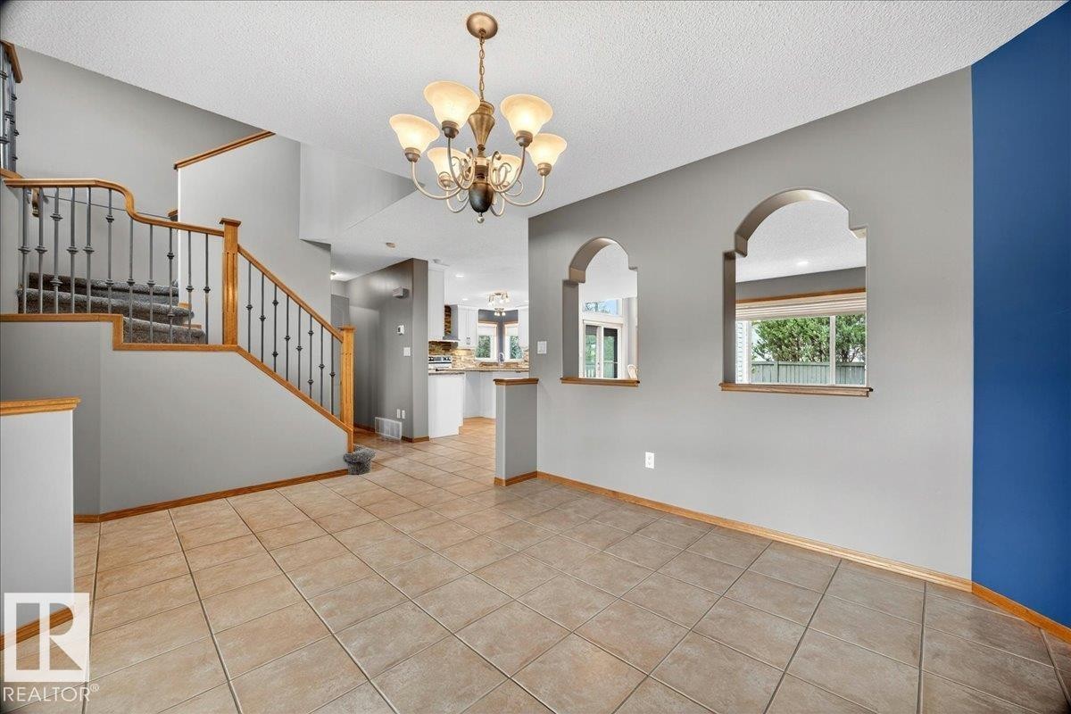 Inviting entry foyer featuring ceramic tile flooring, a carpeted staircase with wood handrails and wrought iron balusters, and a decorative chandelier - 11824 13 Avenue, Edmonton, AB - Indoor Photo Showing Other Room
