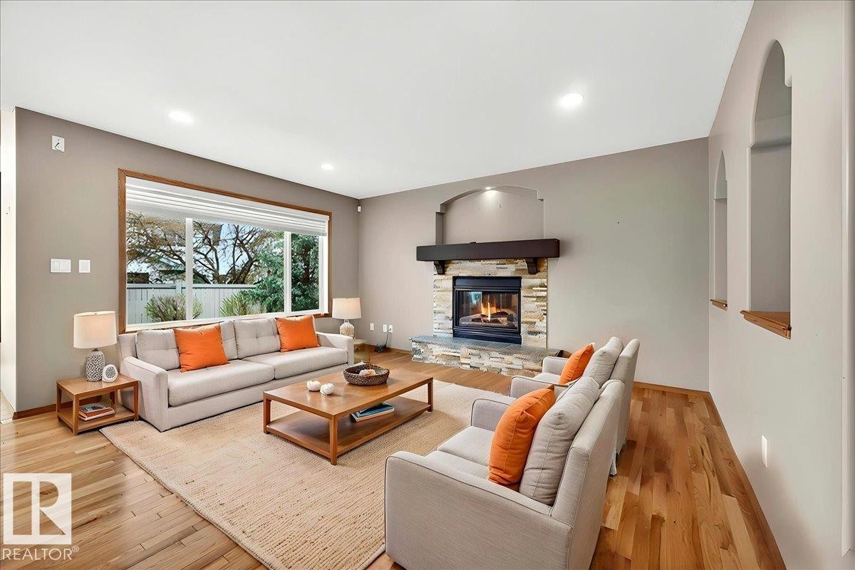 Living area featuring wood-finish flooring, a stone-clad fireplace with a dark wood mantel, and recessed lighting - 11824 13 Avenue, Edmonton, AB - Indoor Photo Showing Living Room With Fireplace