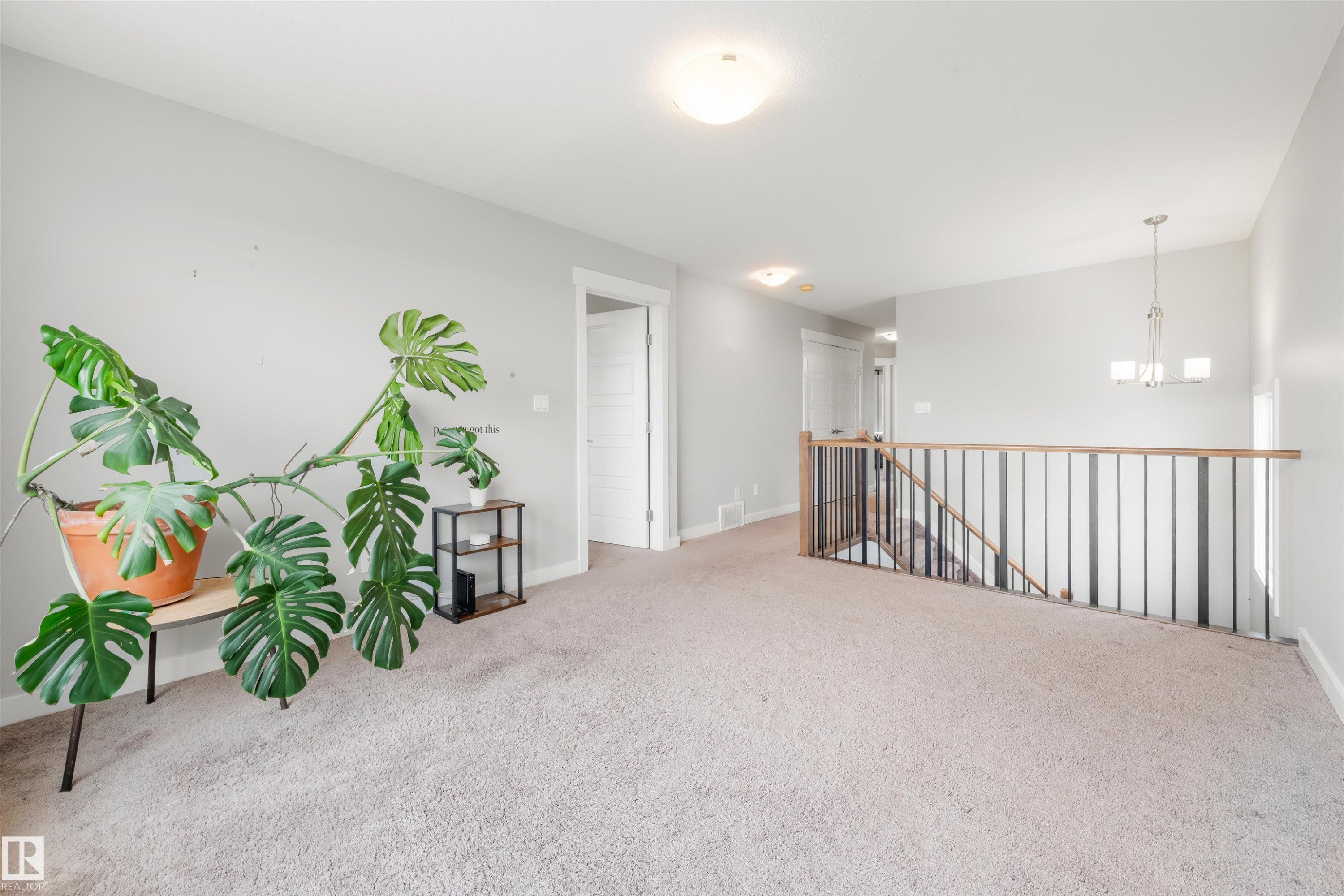 Carpeted area with light gray walls, a staircase with dark balusters and a light wood handrail, and a contemporary chandelier - 607 40 Street Sw, Edmonton, AB - Indoor Photo Showing Other Room