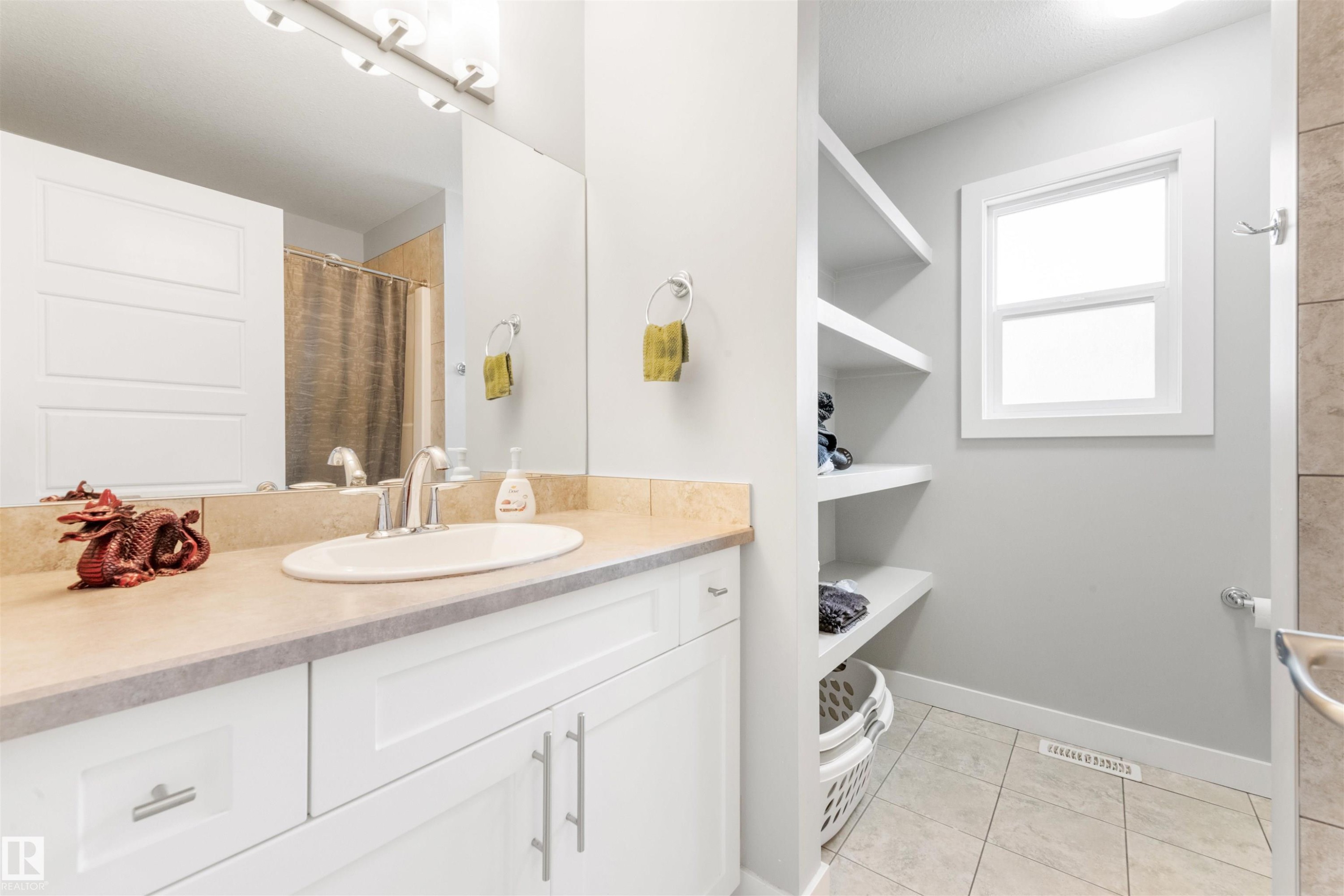 Well-appointed bathroom featuring a vanity with a light-colored countertop and white cabinetry, a large mirror, and open shelving for storage - 607 40 Street Sw, Edmonton, AB - Indoor