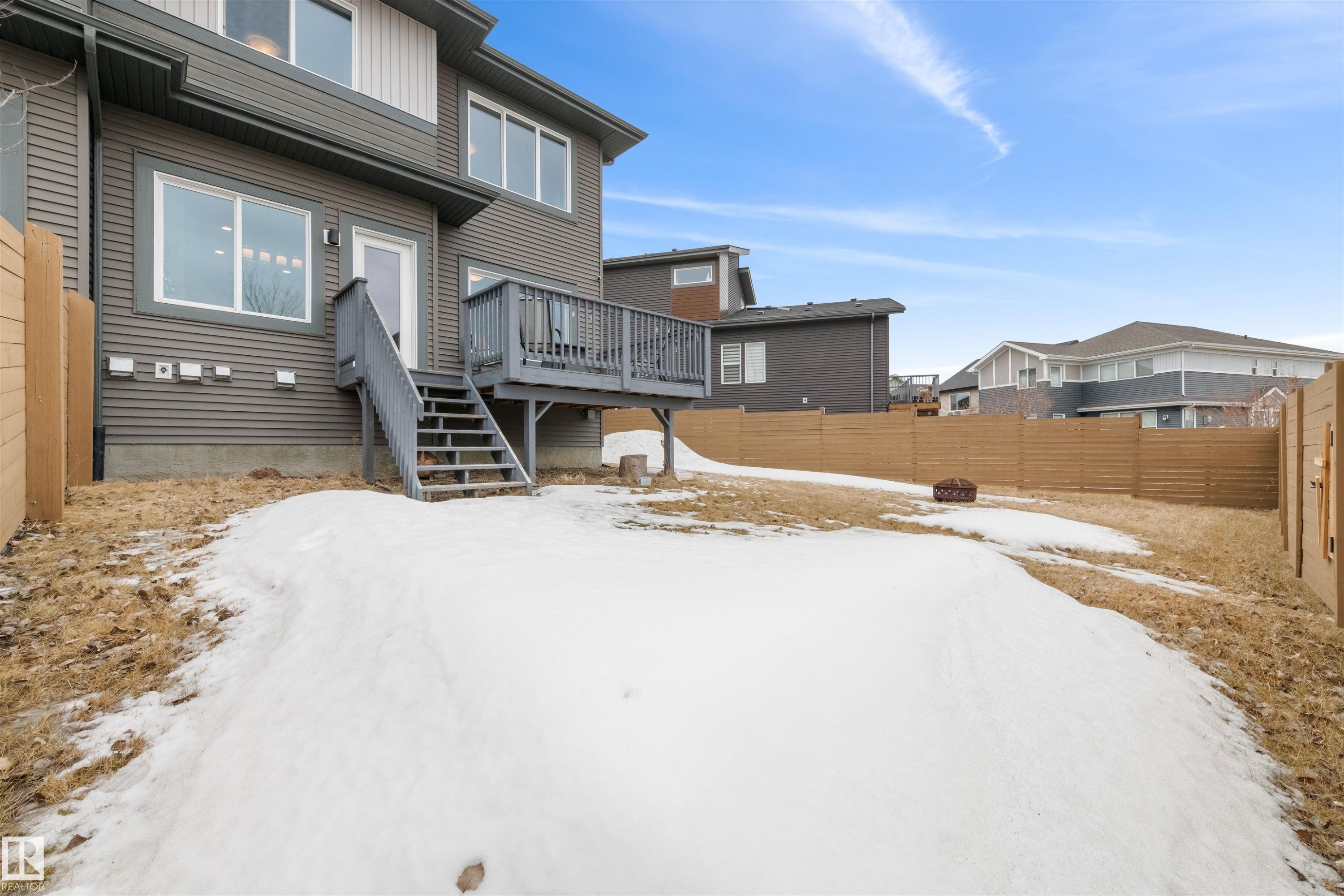 The property features a dark grey exterior with white trim windows and a wooden deck with stairs leading to the backyard - 607 40 Street Sw, Edmonton, AB - Outdoor