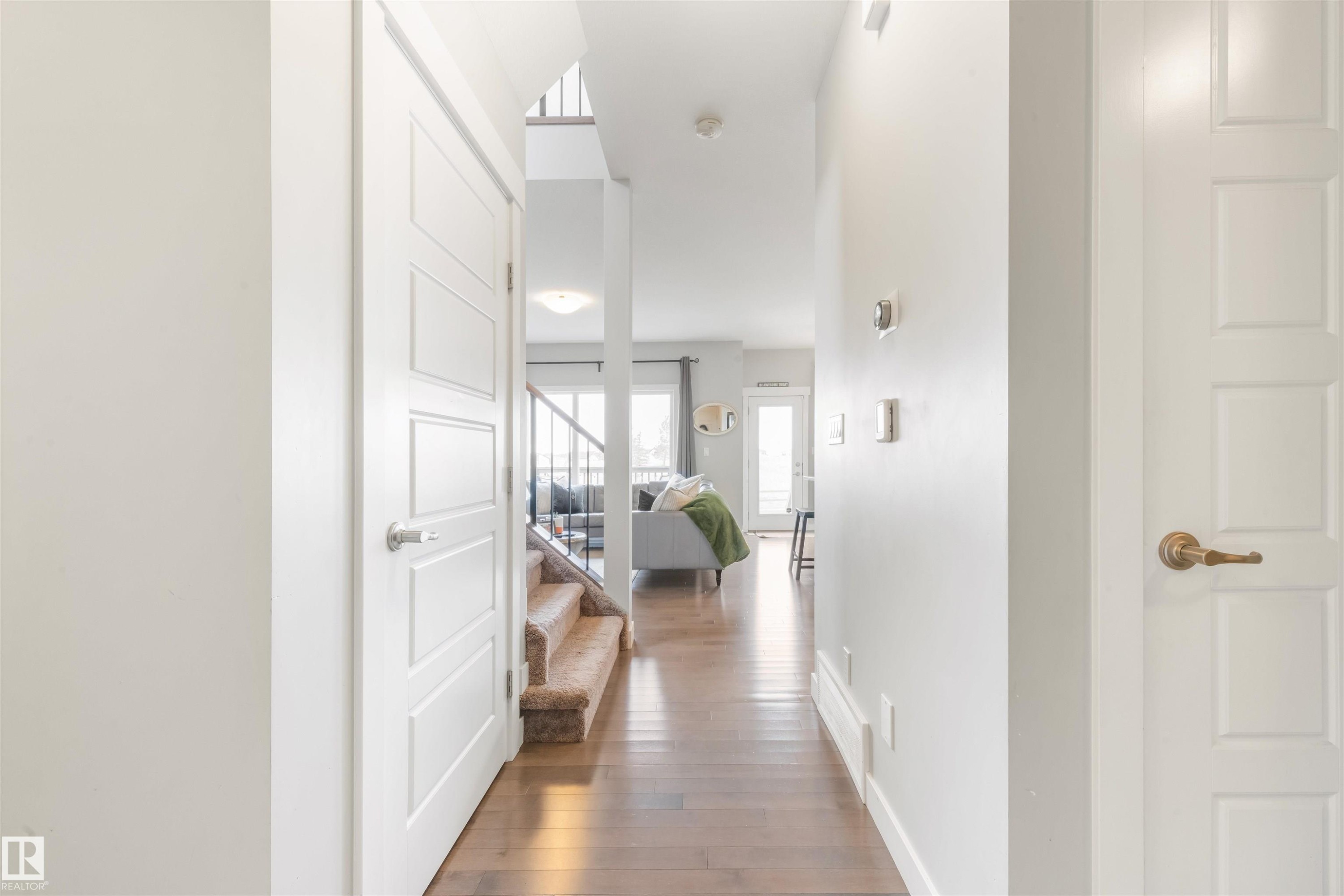 This interior entryway features hardwood flooring and white walls, leading to a carpeted staircase with dark railings - 607 40 Street Sw, Edmonton, AB - Indoor Photo Showing Other Room