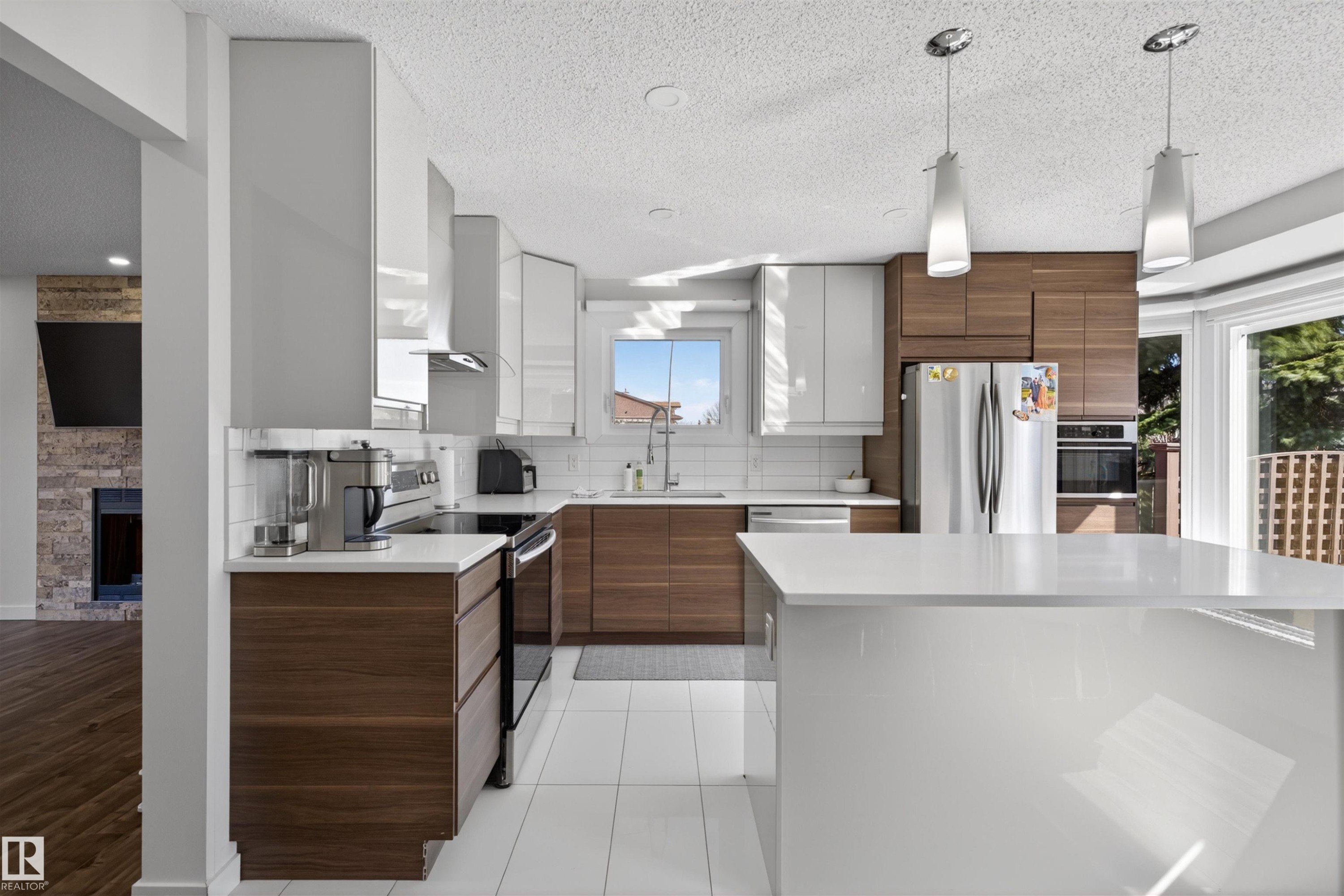Modern kitchen featuring a central island, white subway tile backsplash, stainless steel appliances, and two-tone cabinetry with wood-finish and high-gloss white elements - 15251 88A Street, Edmonton, AB - Indoor Photo Showing Kitchen With Upgraded Kitchen