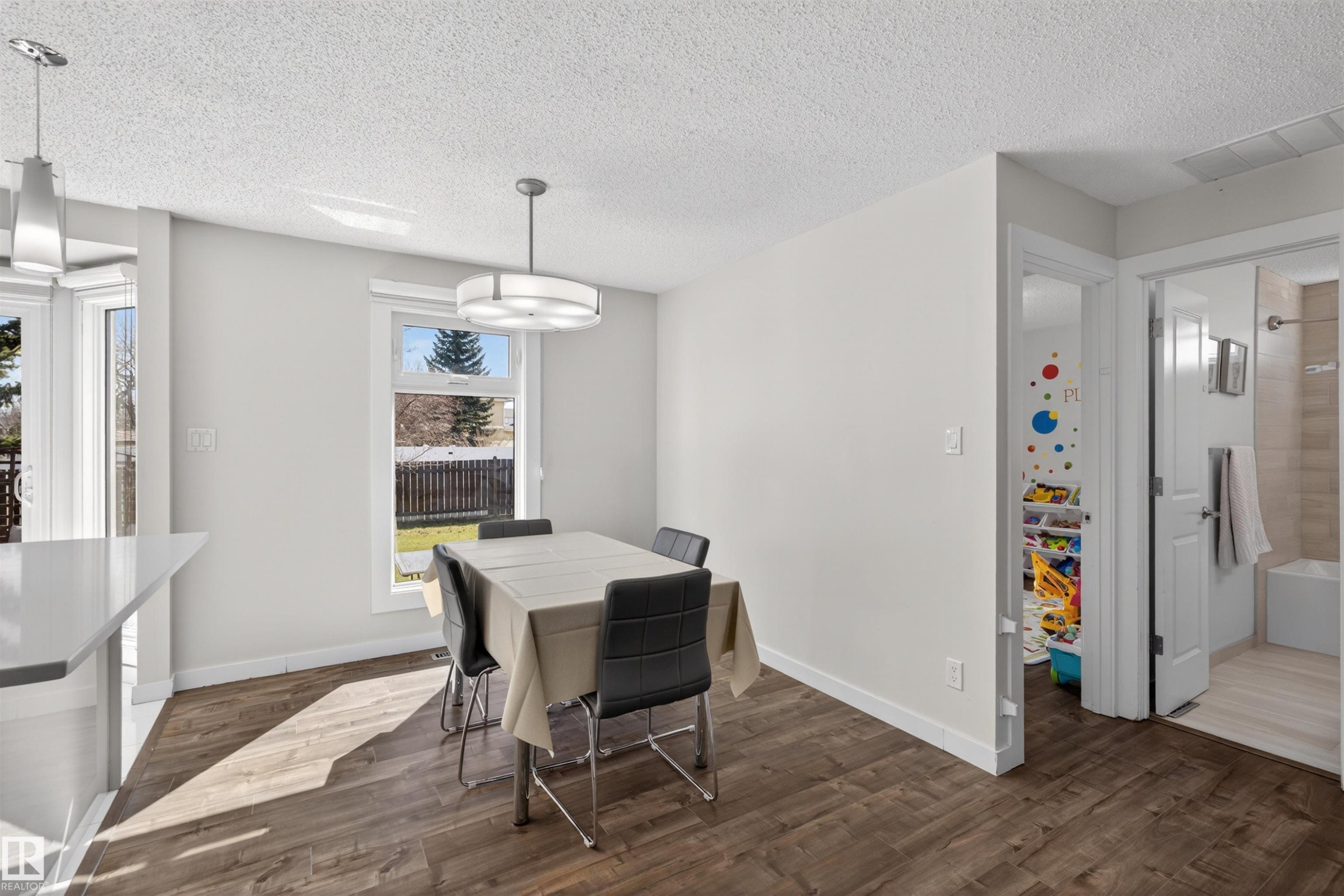 Bright dining area featuring wood-finish flooring, a contemporary ceiling fixture, a window overlooking the backyard, and access to a bathroom with a tiled shower/tub combination - 15251 88A Street, Edmonton, AB - Indoor Photo Showing Dining Room