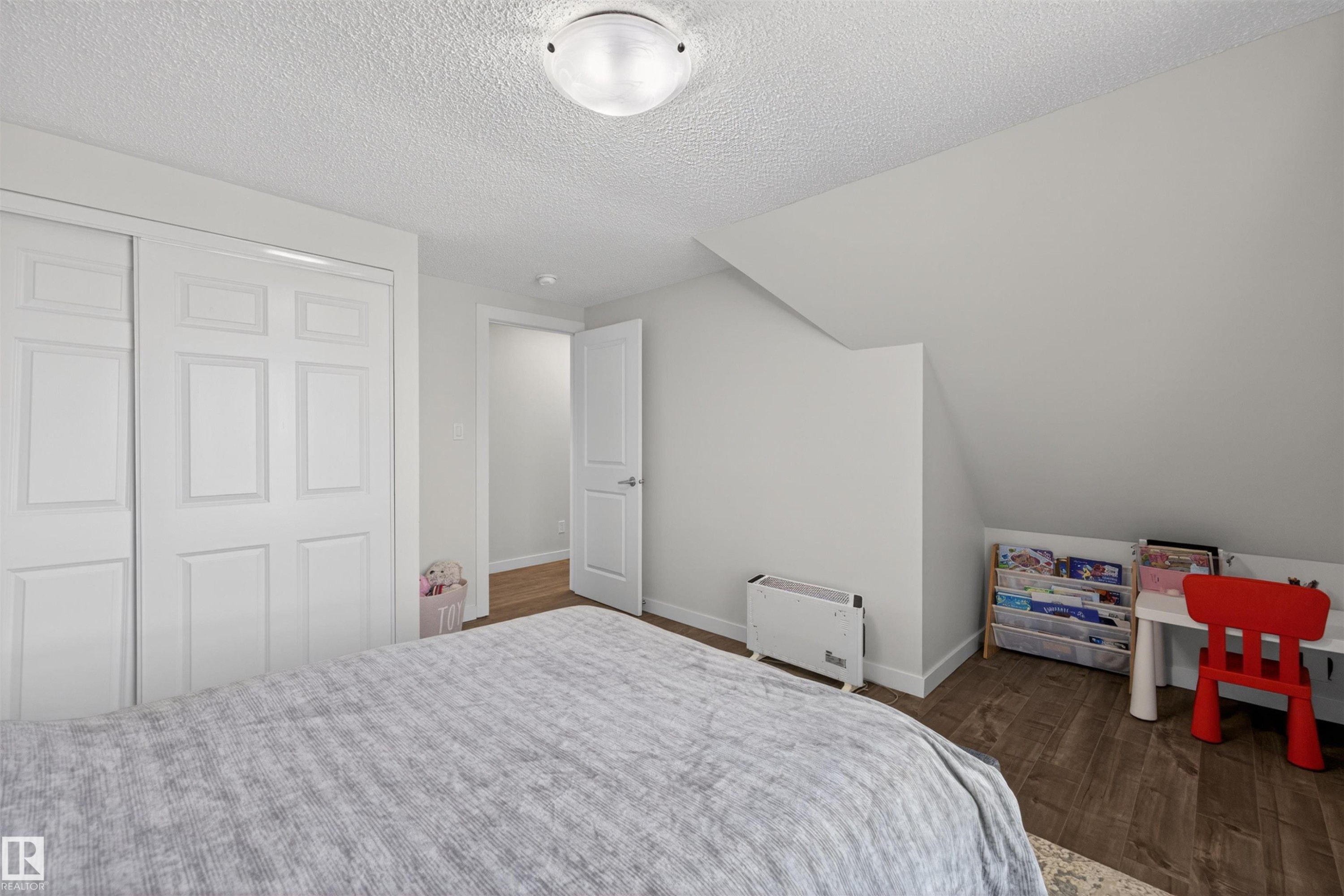 Bedroom featuring wood-finish flooring, white paneled bifold closet doors, a sloped ceiling, and a flush-mount ceiling light fixture - 15251 88A Street, Edmonton, AB - Indoor Photo Showing Bedroom