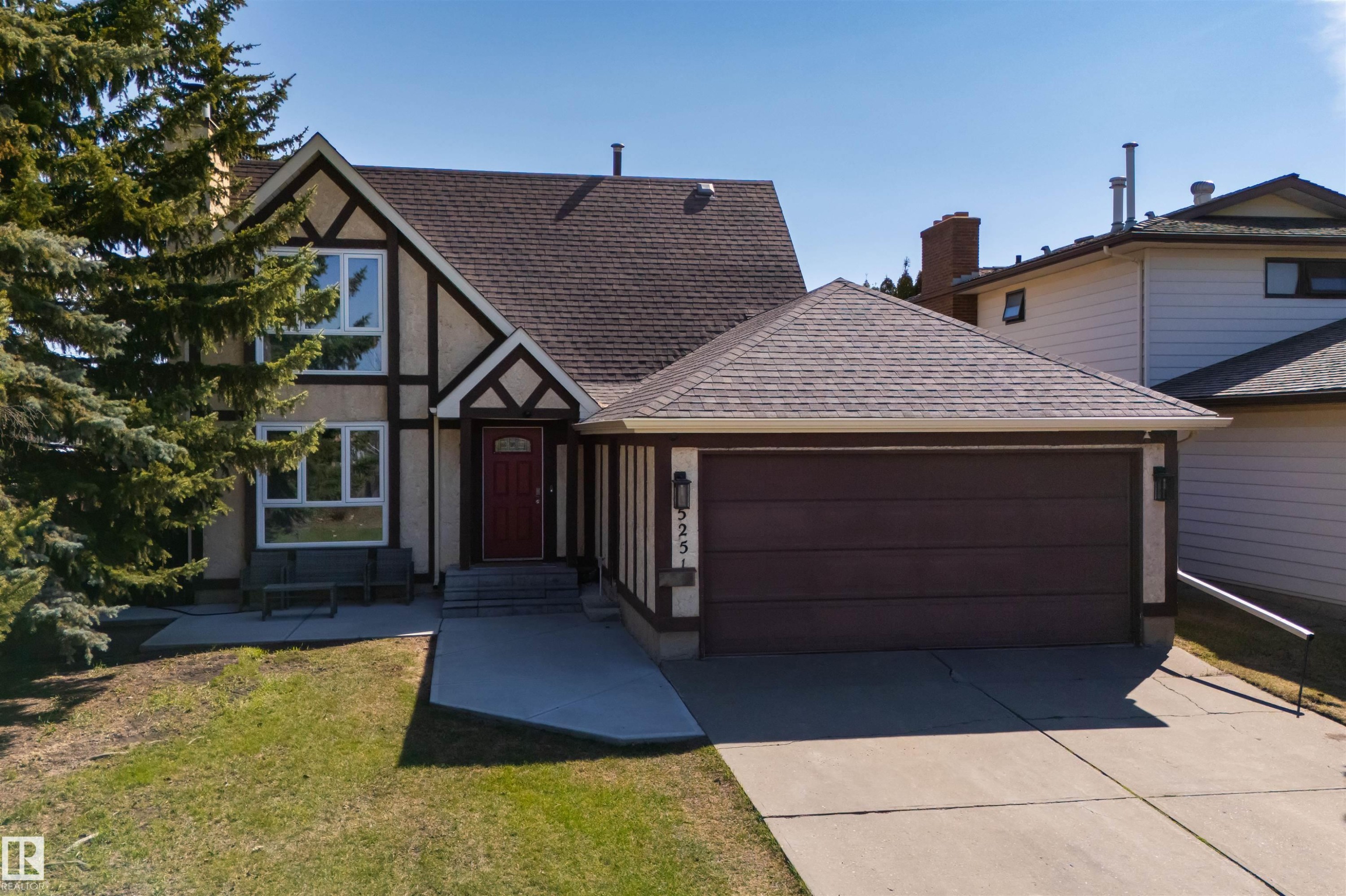 Tudor-style facade with decorative timbering, a prominent red entry door, an attached two-car garage, and a concrete driveway - 15251 88A Street, Edmonton, AB - Outdoor