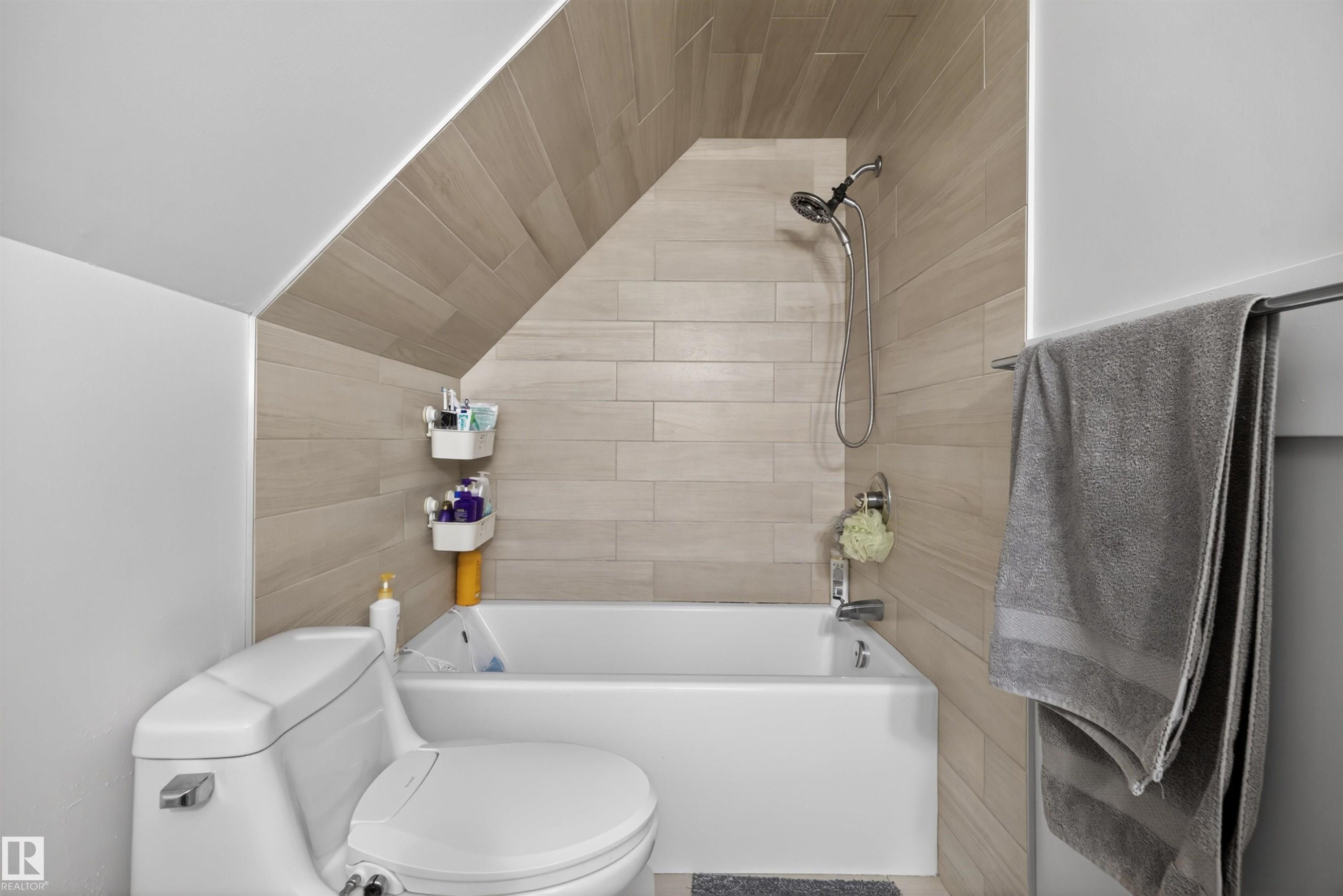 Bathroom featuring a white bathtub, toilet, and tiled walls extending to a sloped ceiling - 15251 88A Street, Edmonton, AB - Indoor Photo Showing Bathroom