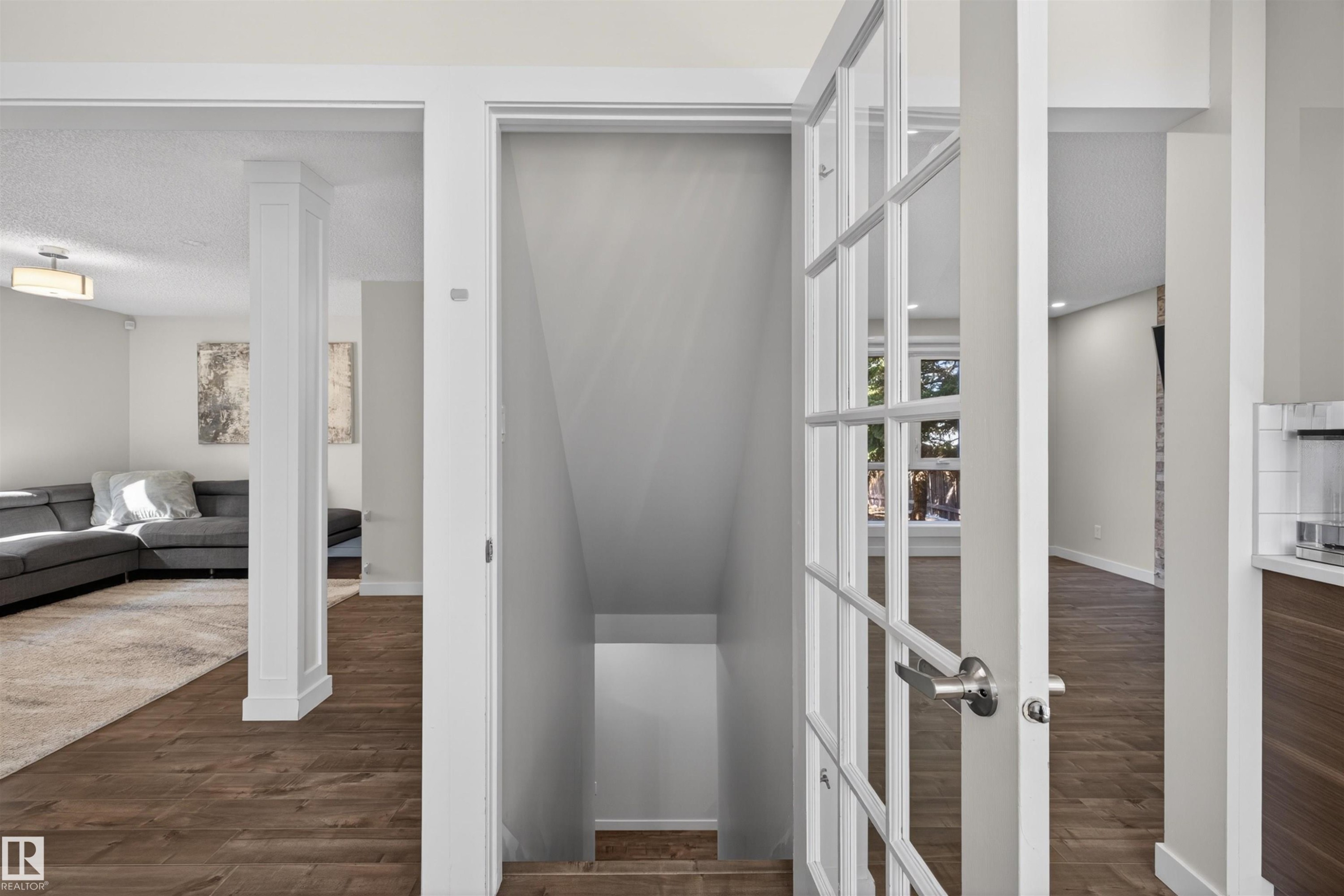 Stairwell entry featuring white French doors with polished chrome hardware, wood-finish flooring, and white baseboards - 15251 88A Street, Edmonton, AB - Indoor Photo Showing Other Room
