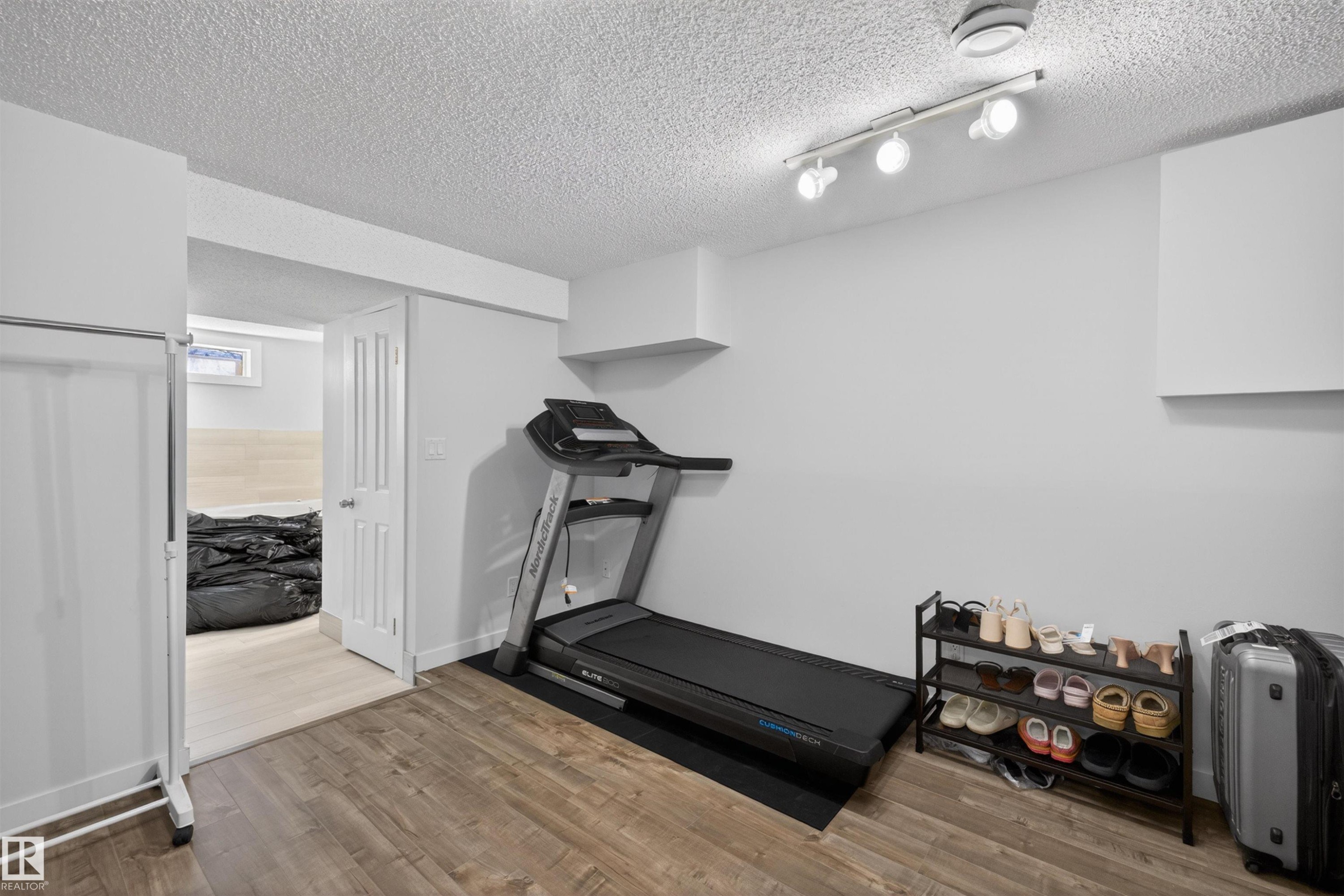 Finished basement room featuring wood-finish flooring, white painted walls, and track lighting - 15251 88A Street, Edmonton, AB - Indoor Photo Showing Gym Room
