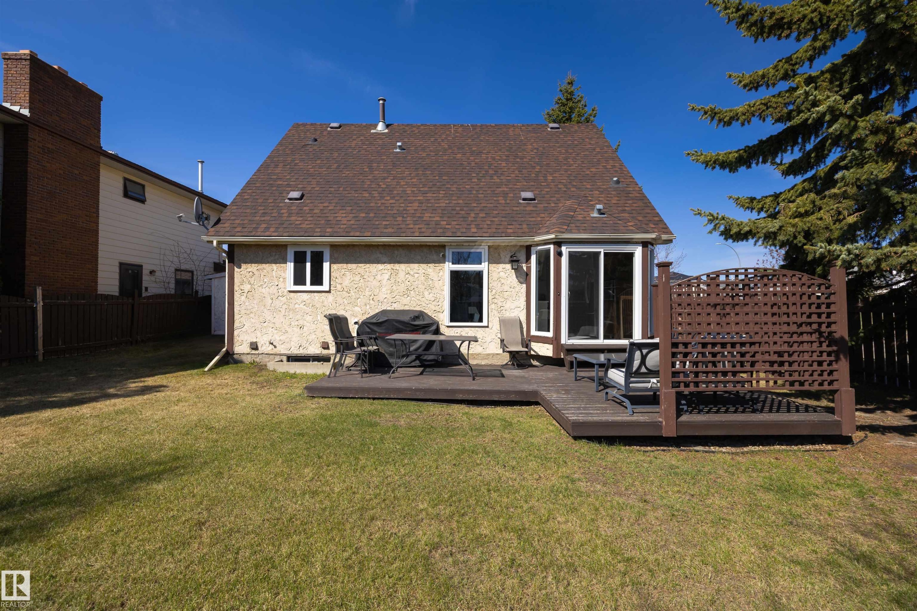 Expansive rear yard featuring a dark wood-finish deck with privacy lattice, a bay window, and sliding glass door access to the interior - 15251 88A Street, Edmonton, AB - Outdoor With Exterior
