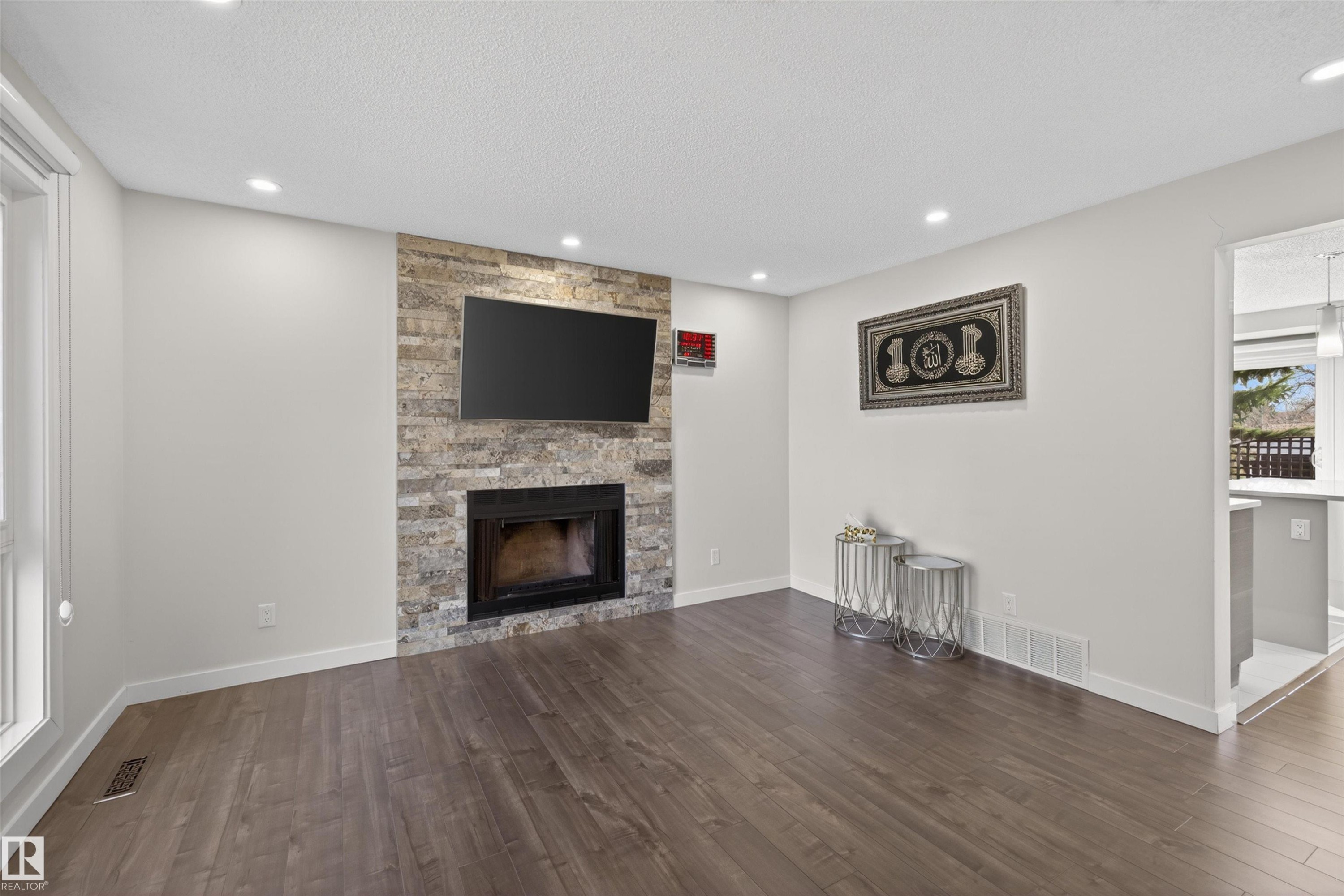Living area featuring a stone accent wall with a built-in fireplace, wood-finish flooring, recessed lighting, and white baseboards - 15251 88A Street, Edmonton, AB - Indoor Photo Showing Living Room With Fireplace
