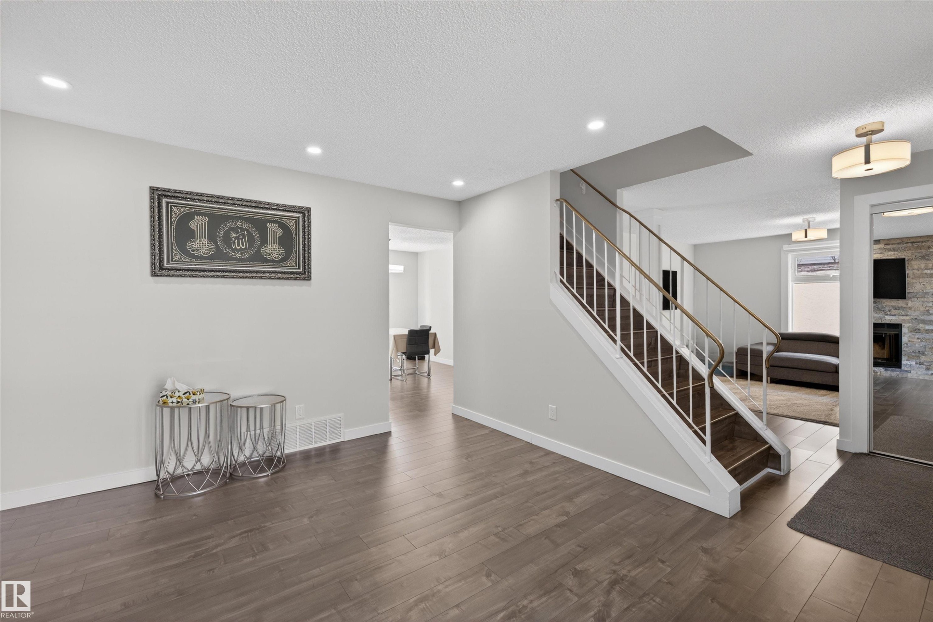 Hardwood-finish flooring extends throughout this entry area, featuring a staircase with white risers and a dark wood-finish tread - 15251 88A Street, Edmonton, AB - Indoor